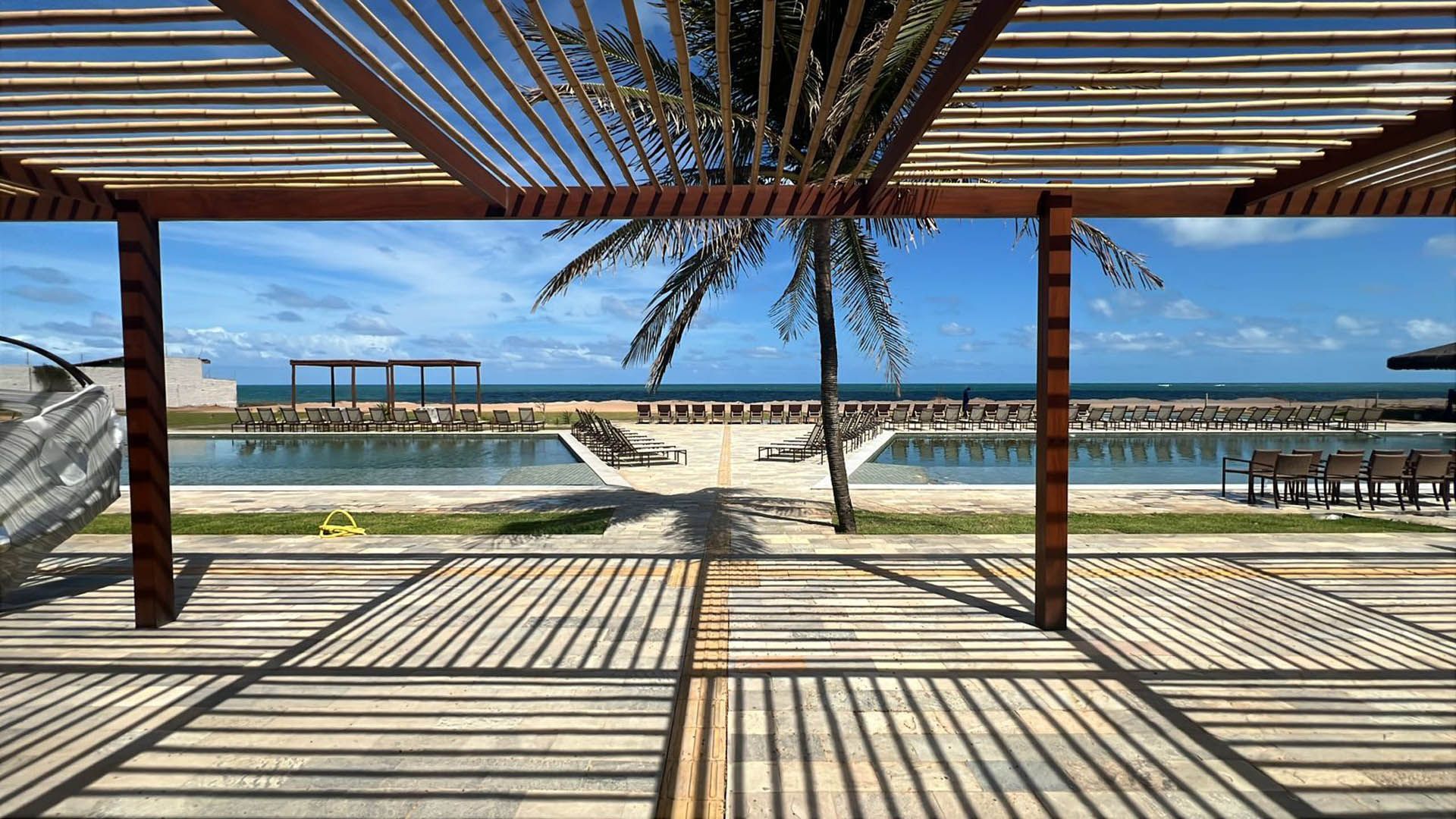 Pérgola de praia com cobertura listrada, vista para o mar e espreguiçadeiras em um dia ensolarado.