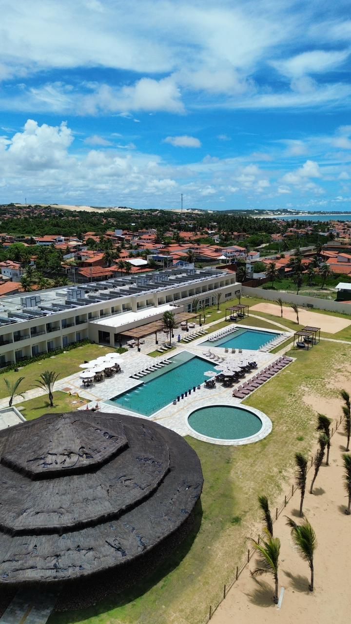 Piscina do resort e pátio ajardinado ao lado de prédios baixos sob um céu azul brilhante.