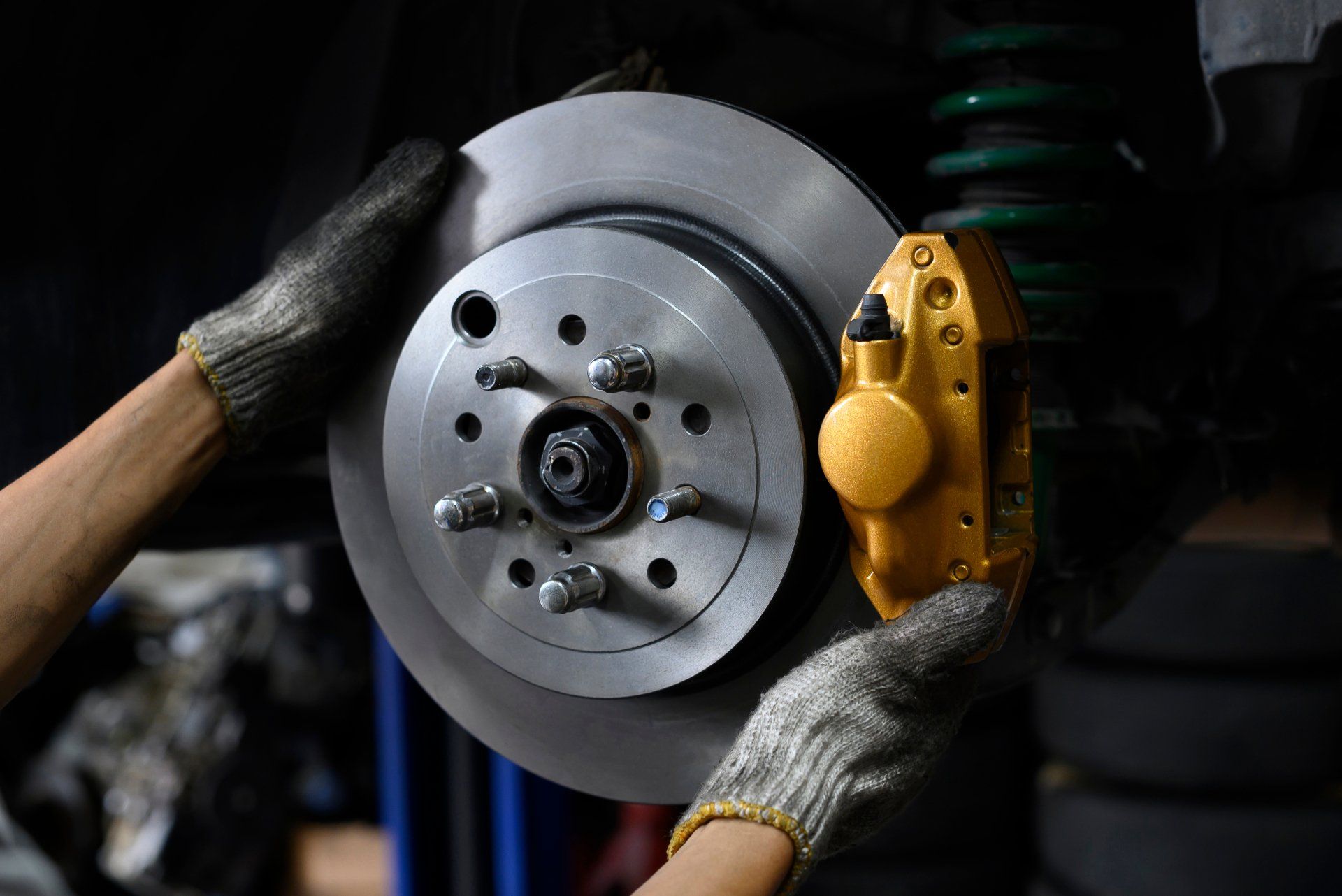 Hands with gloves installing a car brake rotor and caliper.