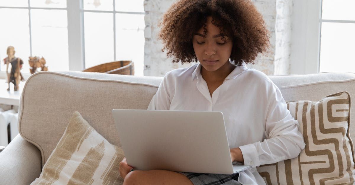 A woman is sitting on a couch using a laptop computer.