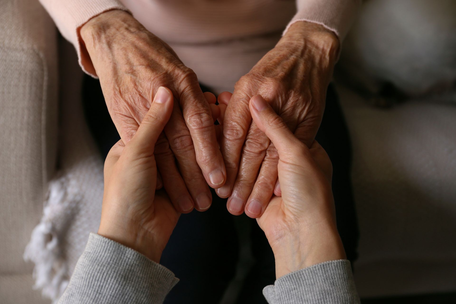 Close-up, high-angle view of two hands holding the weathered, wrinkled hands of another person in a gesture of support. Close-up, high-angle view of two hands holding the weathered, wrinkled hands of another person in a gesture of support.