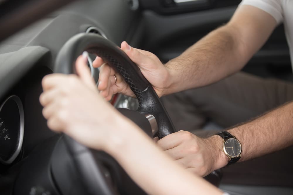 Female and Male Hands Handling Steering Wheel — Howards Professional Driving School In Gordonvale, QLD