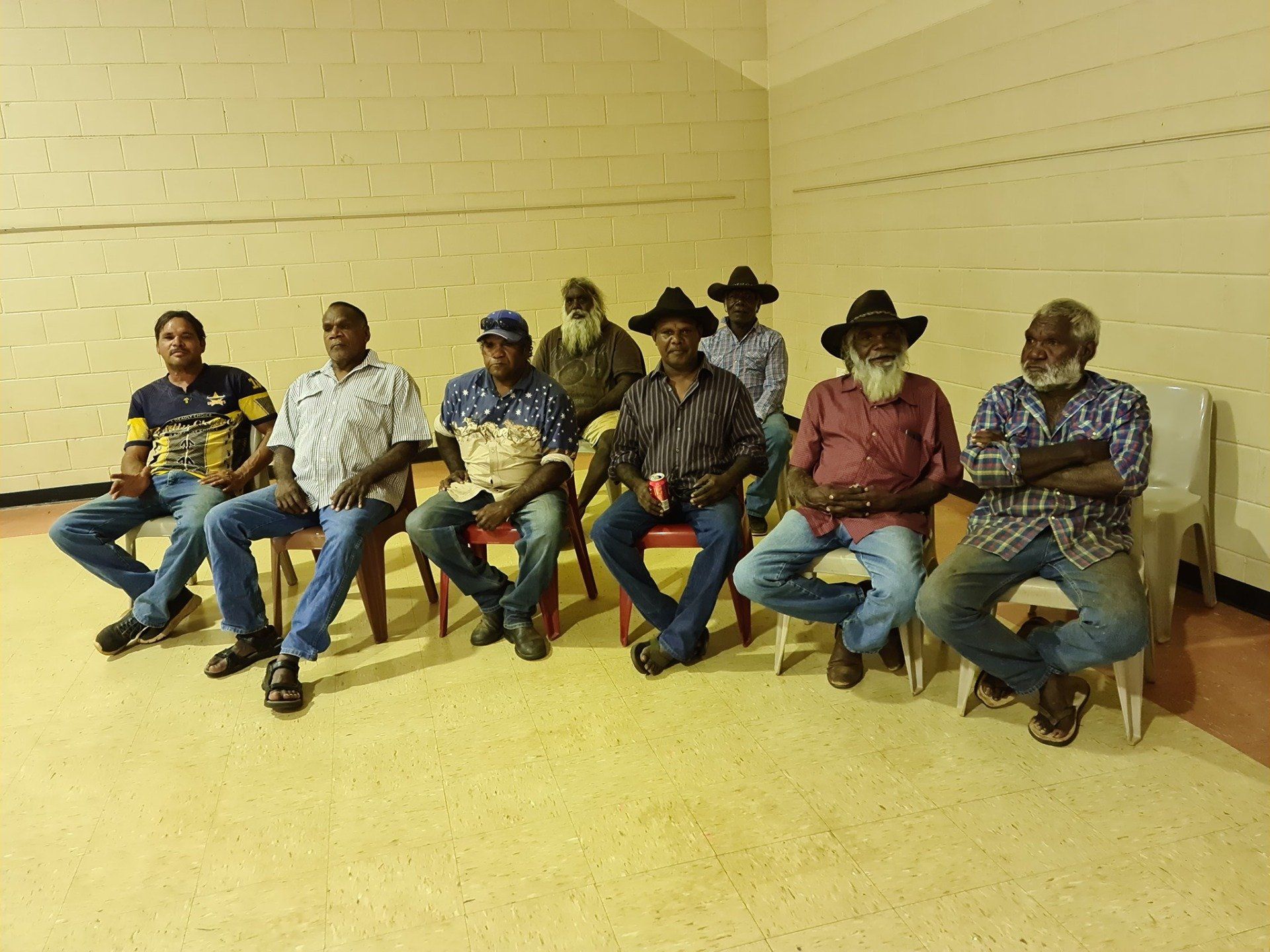 A group of ten men in casual attire seated on chairs indoors, likely at a meeting.