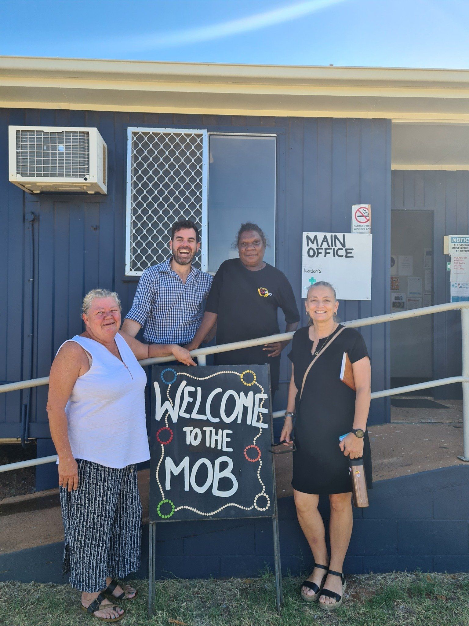 Four people stand in front of a blue building, one holding a 
