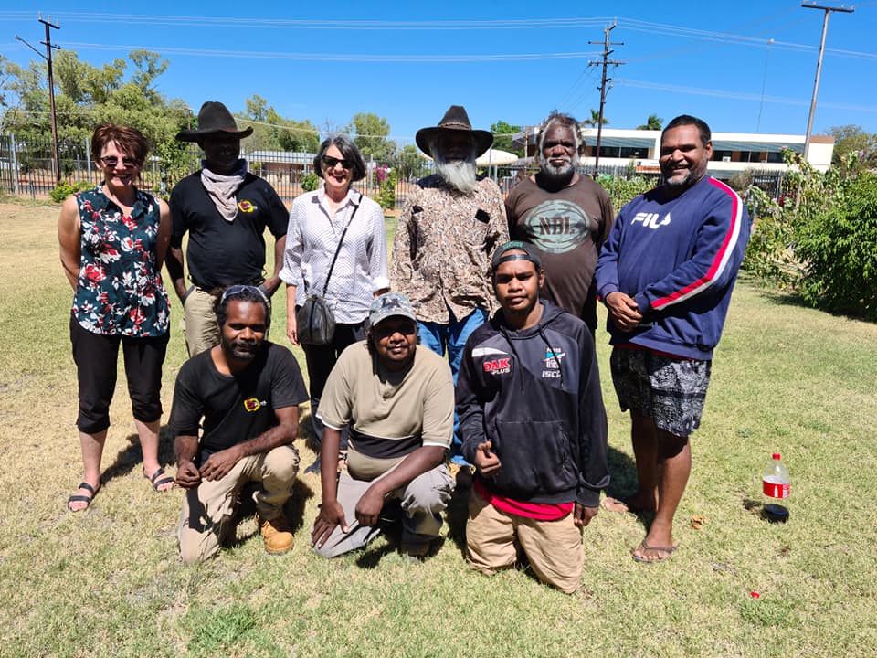 Group of ten people, diverse ages and ethnicities, standing and kneeling outdoors on a sunny day.