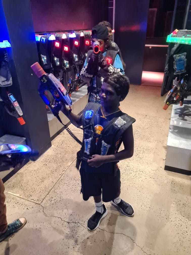 Two kids at a laser tag arena, wearing vests and holding laser guns.