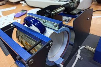 Close-up of a blue-and-black handheld machine with a white tape roll and metal rollers on a workbench