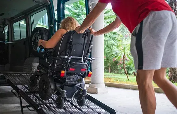 Pushing a woman in a wheelchair into a van.