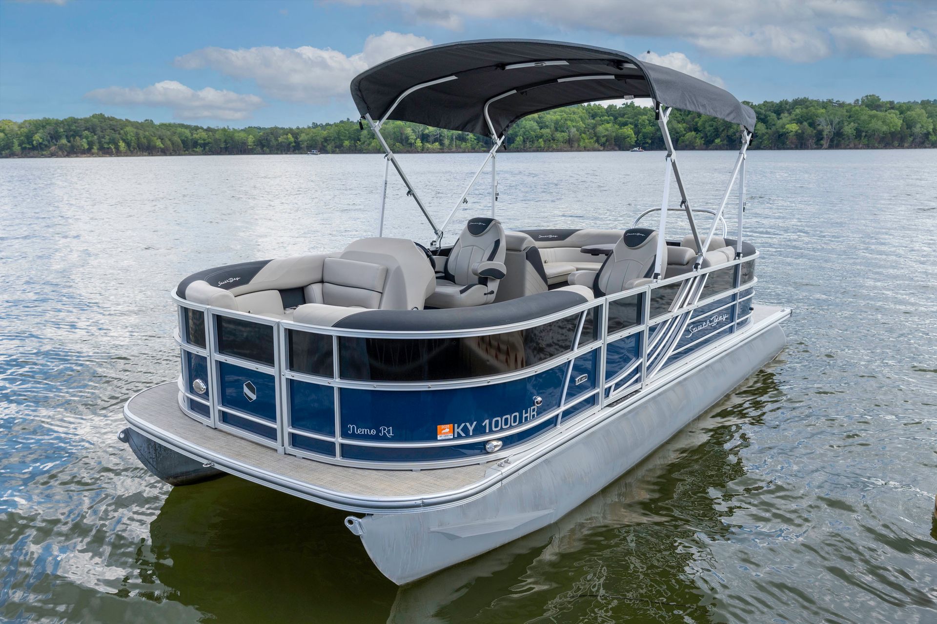 A pontoon boat is parked on a trailer in a grassy field.