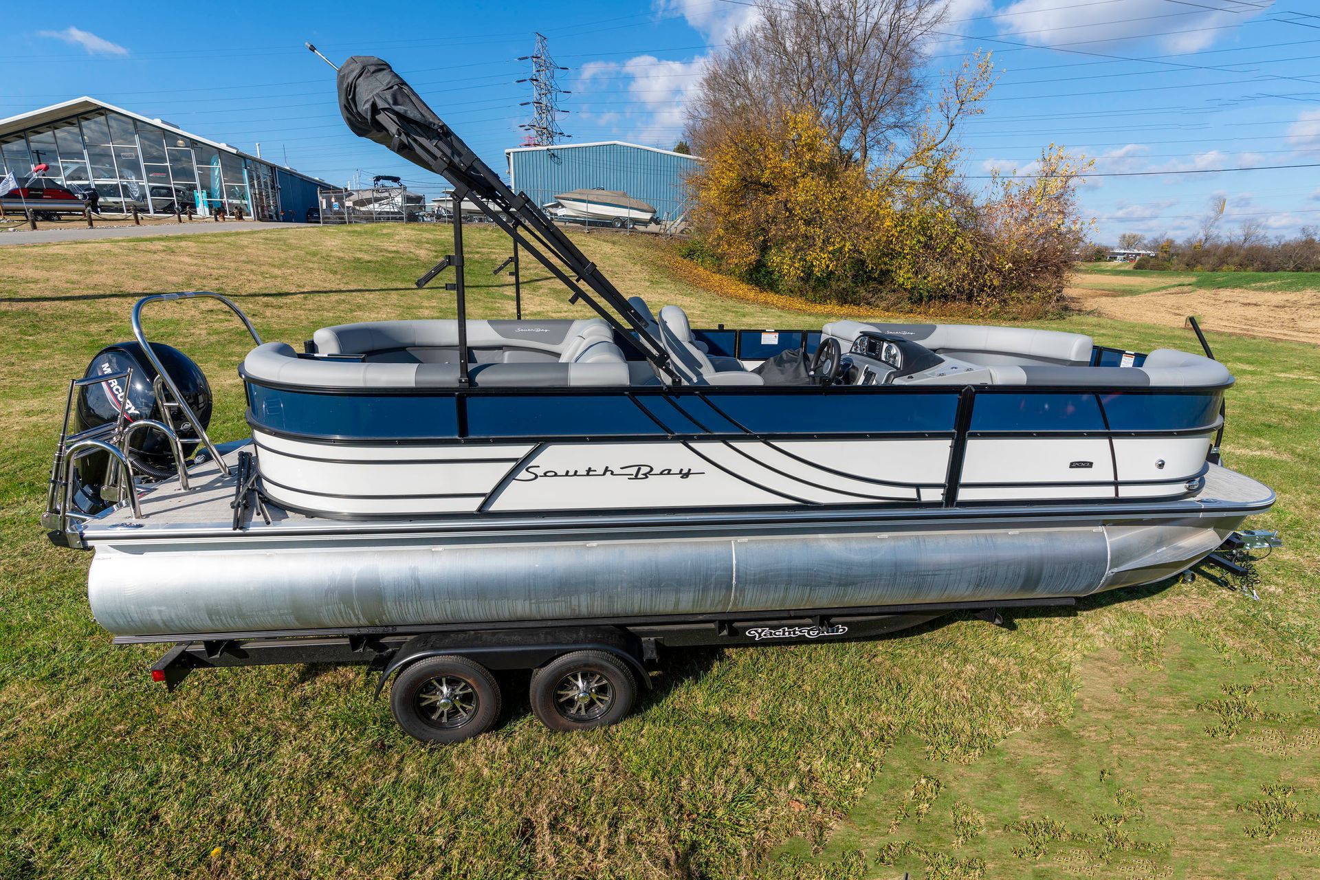 A pontoon boat is parked on a trailer in a grassy field.