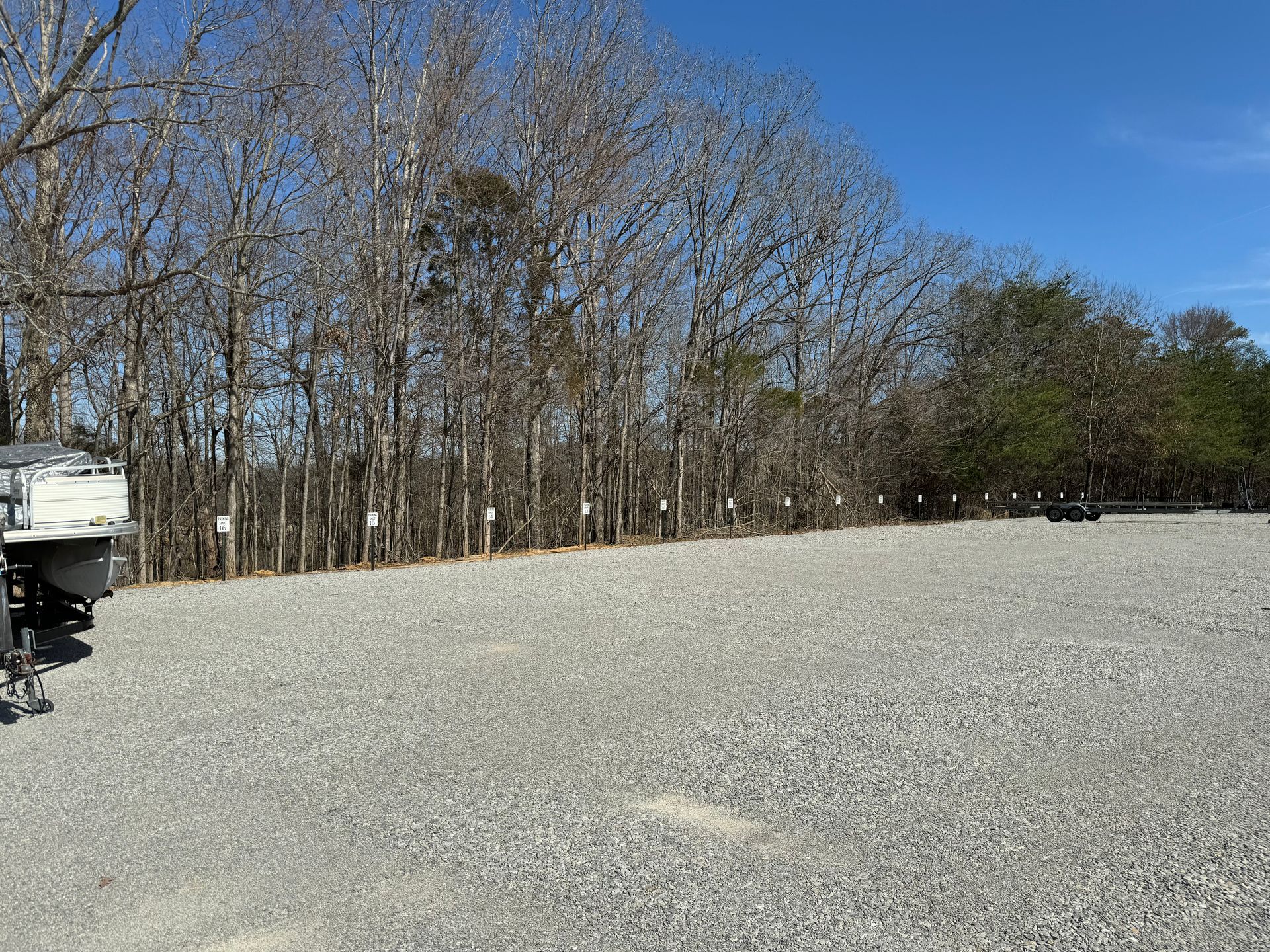 A boat is parked in a gravel lot with trees in the background.