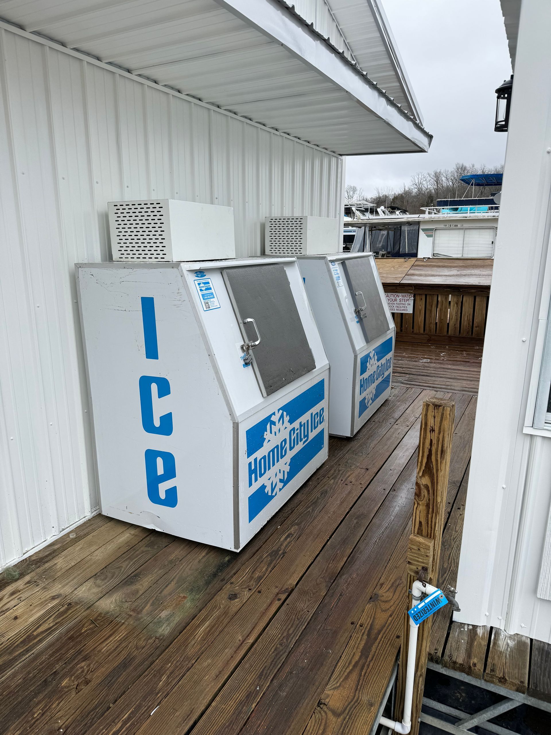 Two ice machines are sitting on a wooden deck outside of a building.