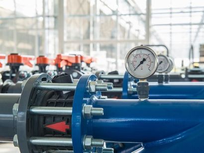 A row of blue pipes with pressure gauges attached to them in a factory.