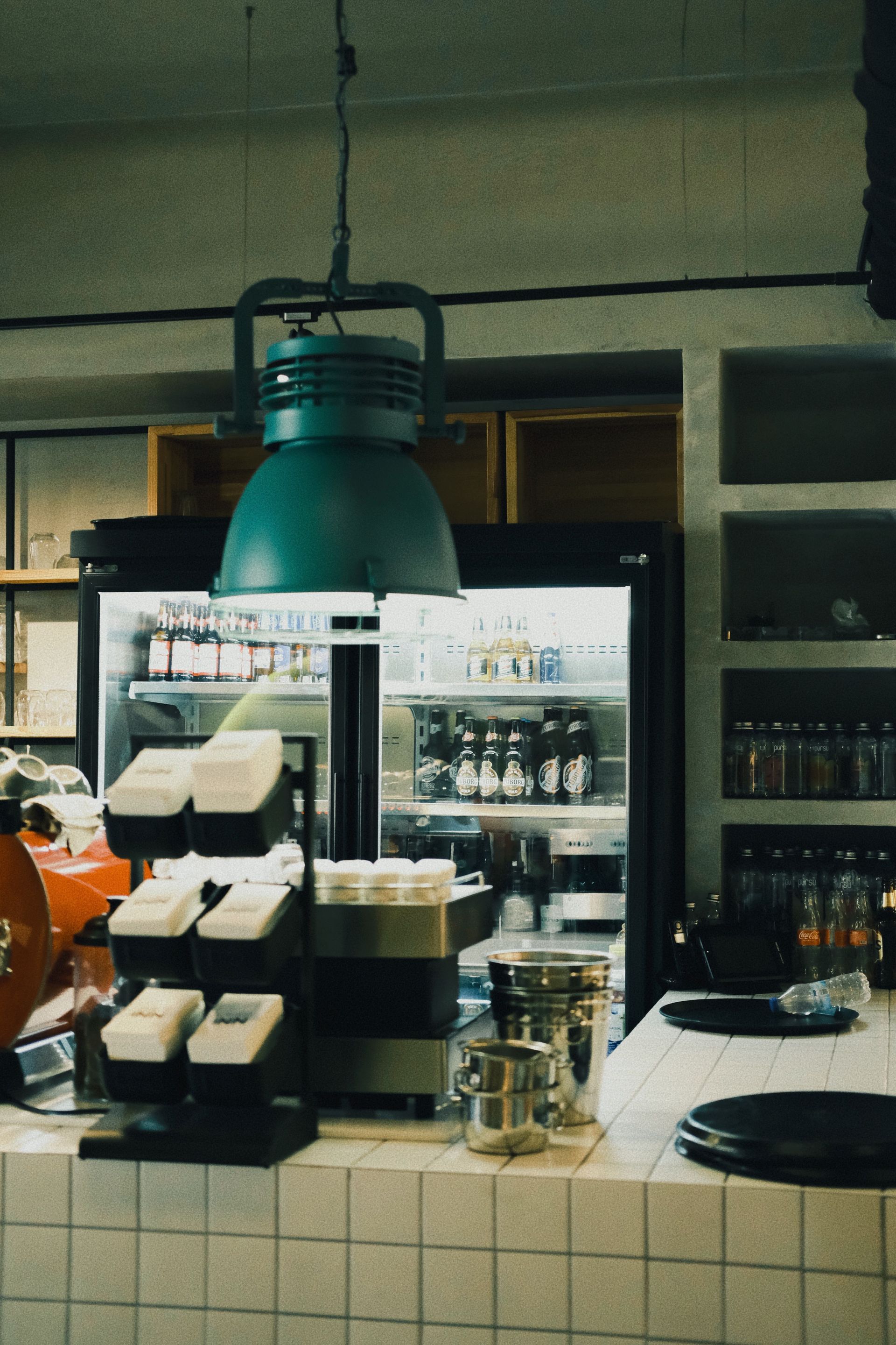 Coffee shop counter with pastries, drinks, and a large green hanging lamp under dim lighting