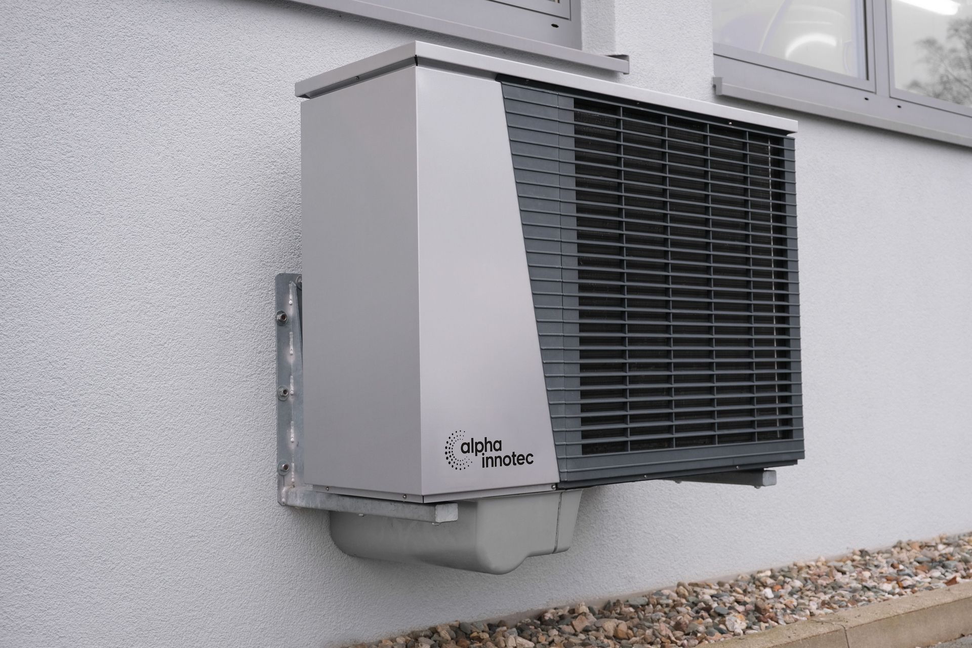 Wall-mounted outdoor air conditioning unit beside a house exterior wall