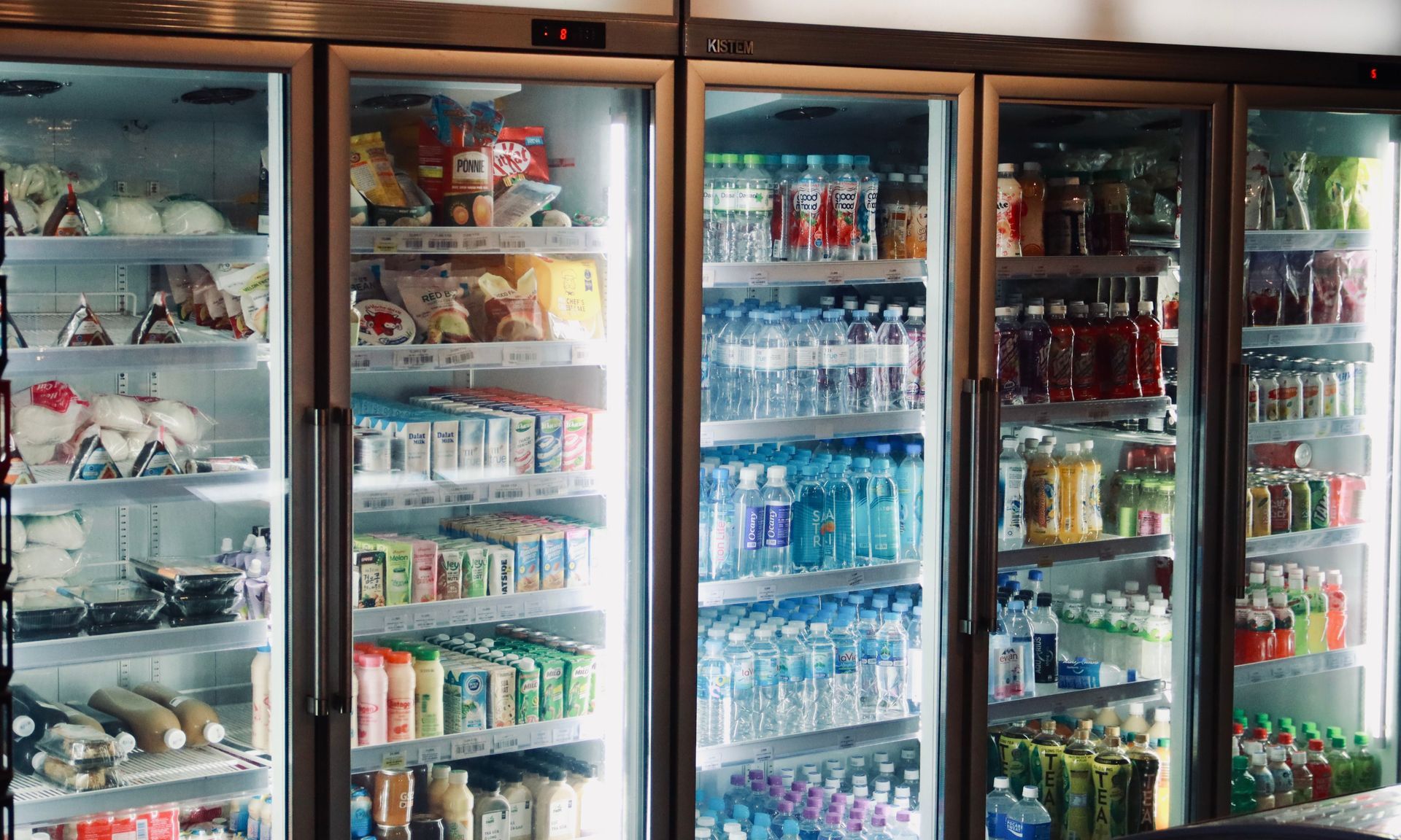 Refrigerated store coolers stocked with drinks, snacks, and dairy items behind glass doors