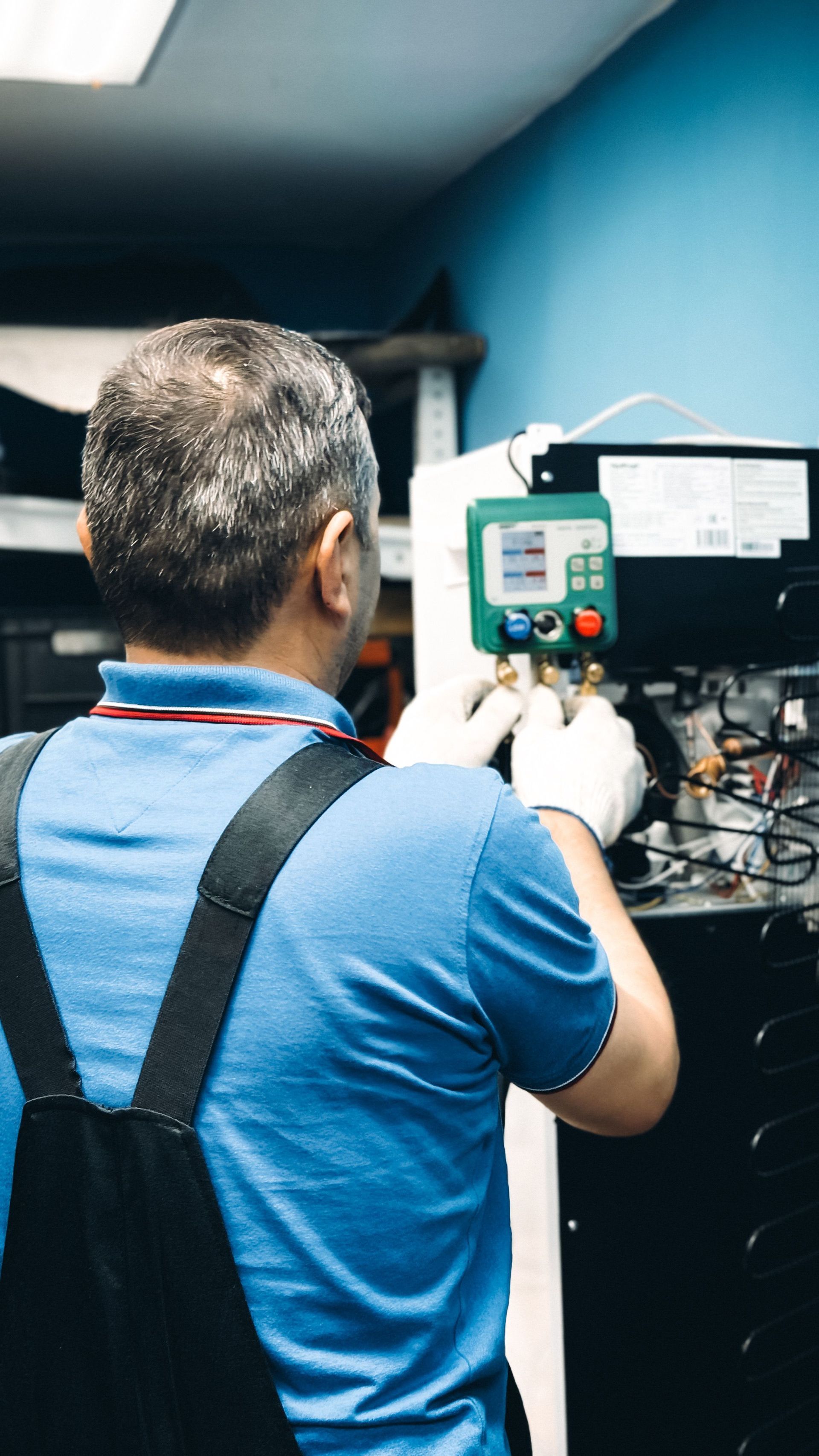 Technician in blue shirt inspecting a control panel inside a utility room