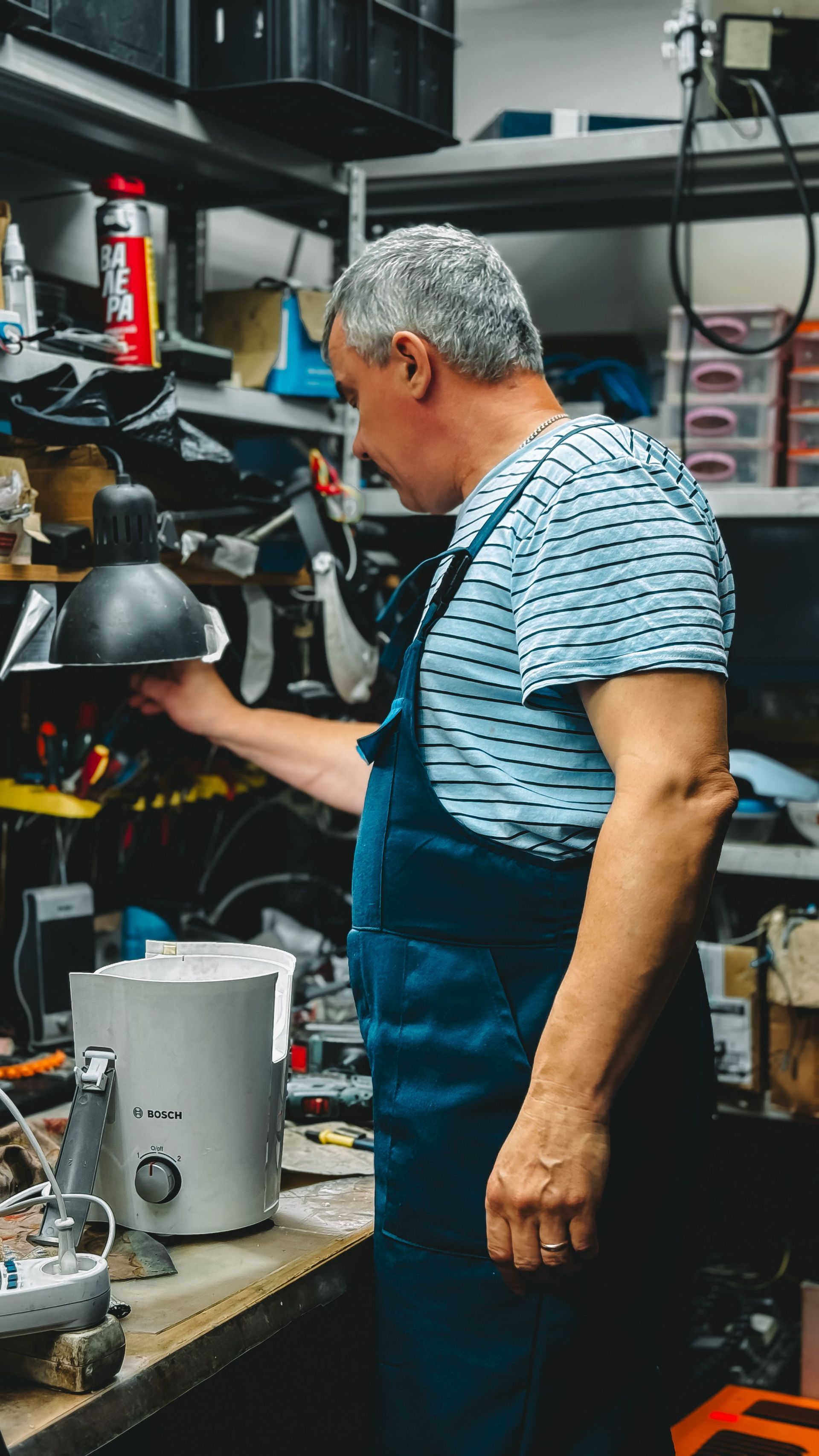 Person in blue apron working at a cluttered workshop bench with tools and equipment.