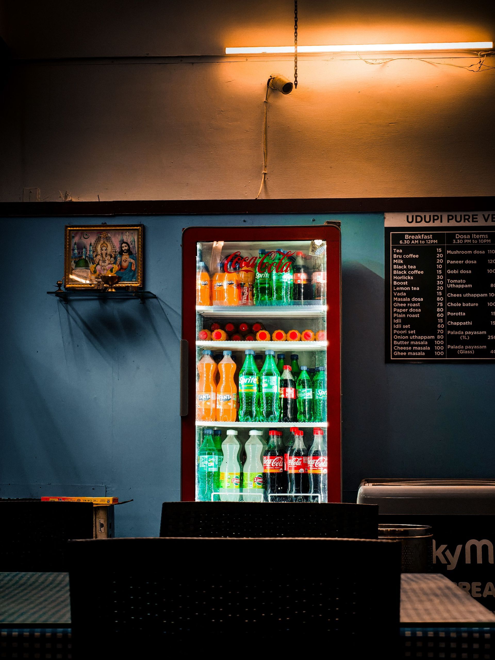 Cozy bar interior with a lit glass-door fridge of colorful drinks and a menu board on the wall