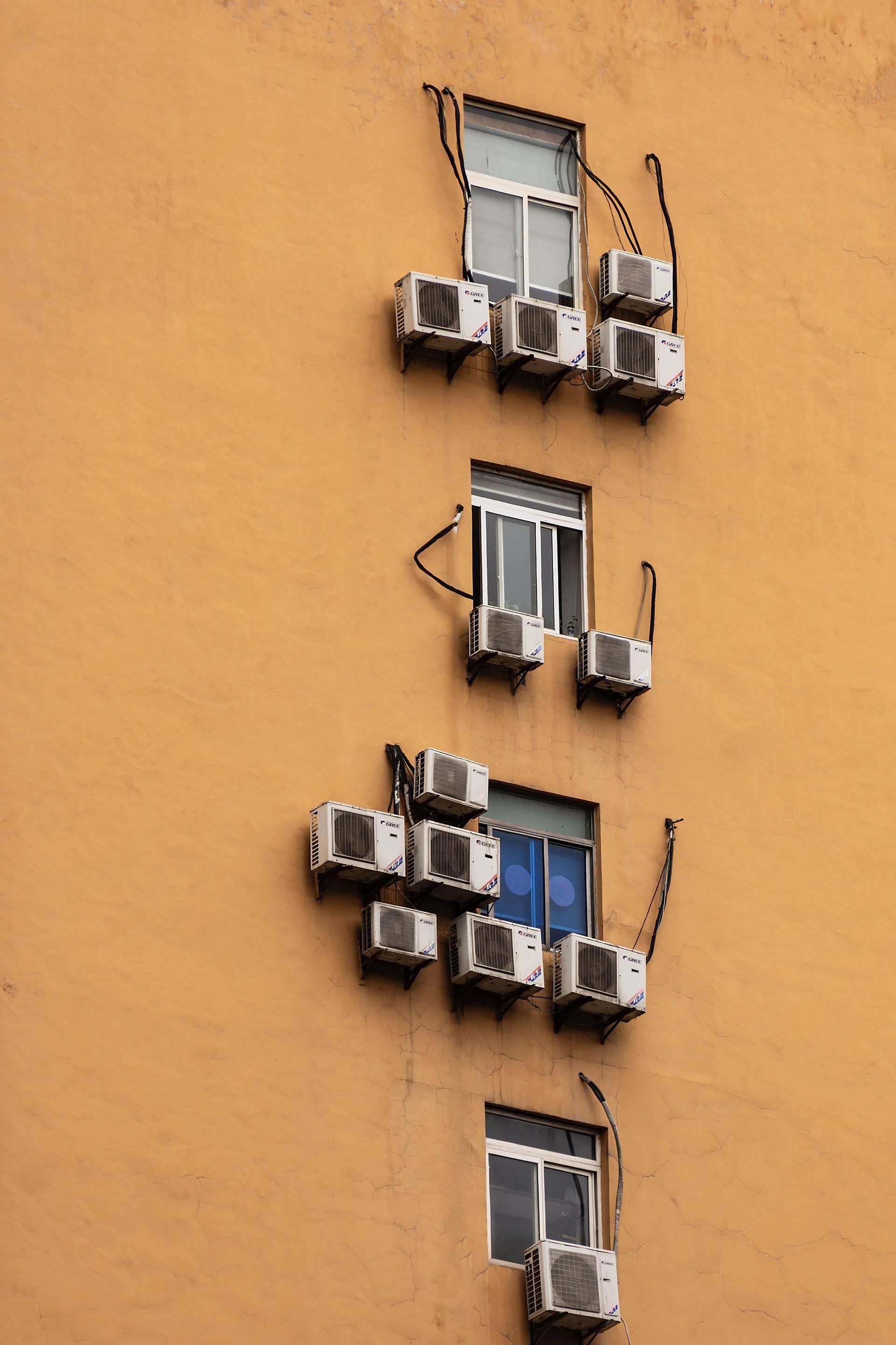 Orange building wall with several windows and air-conditioning units mounted beneath them