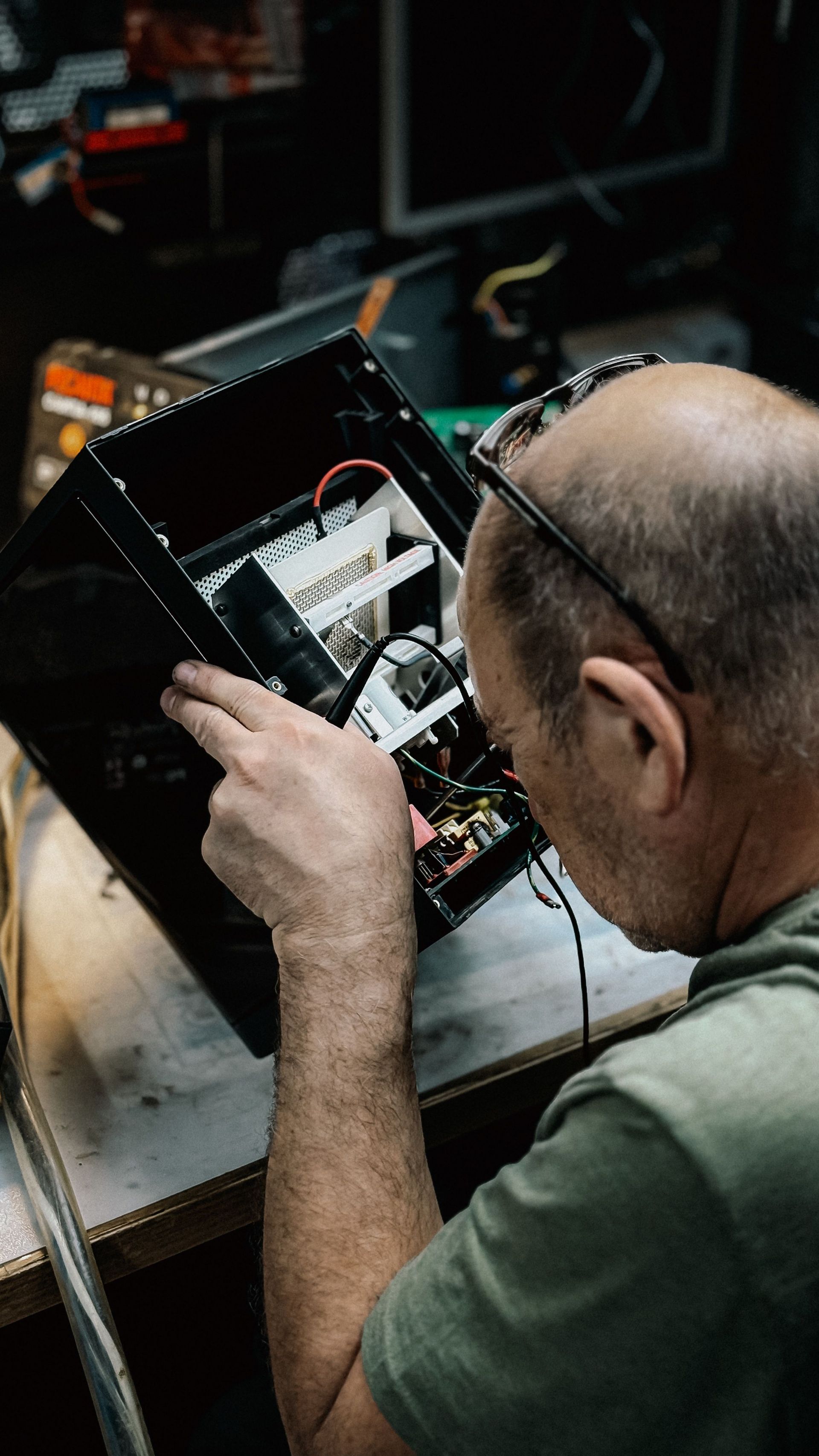 Technician inspecting a circuit board on a workbench with tools and a laptop nearby