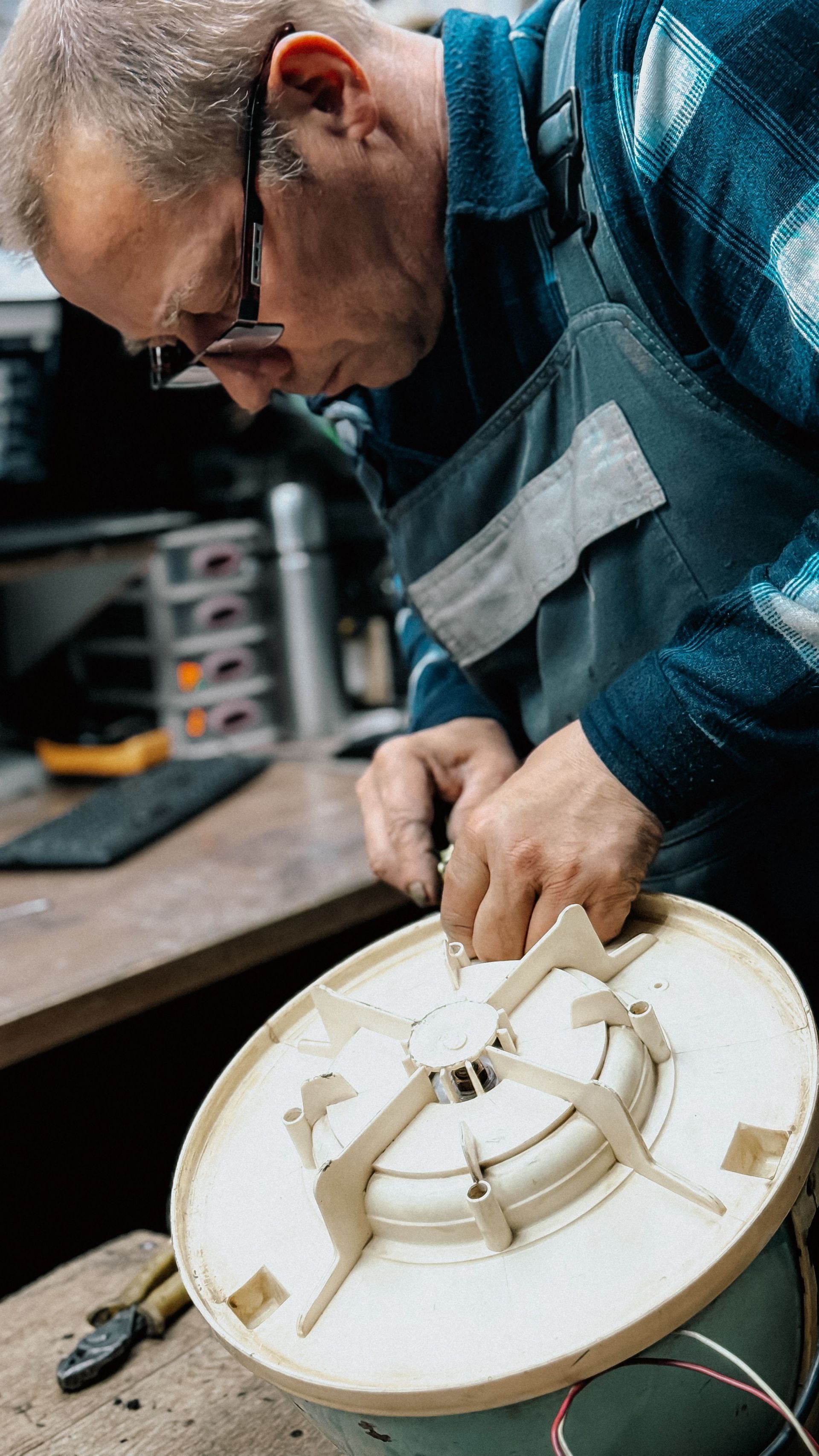 Man repairing a white circular device on a workbench in a workshop, leaning close with tools nearby