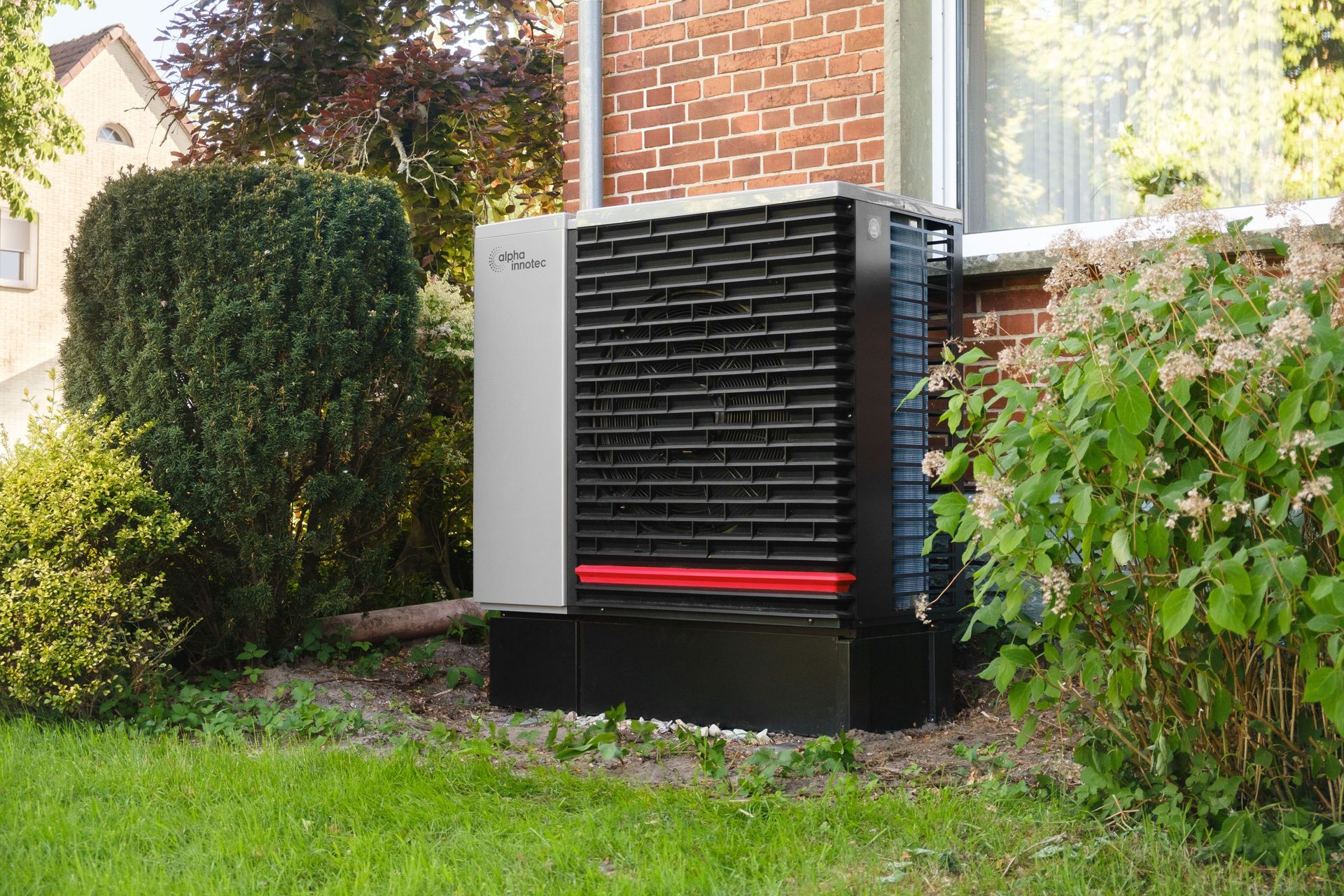 Outdoor HVAC unit beside a brick house, partially hidden by hedges and lawn greenery