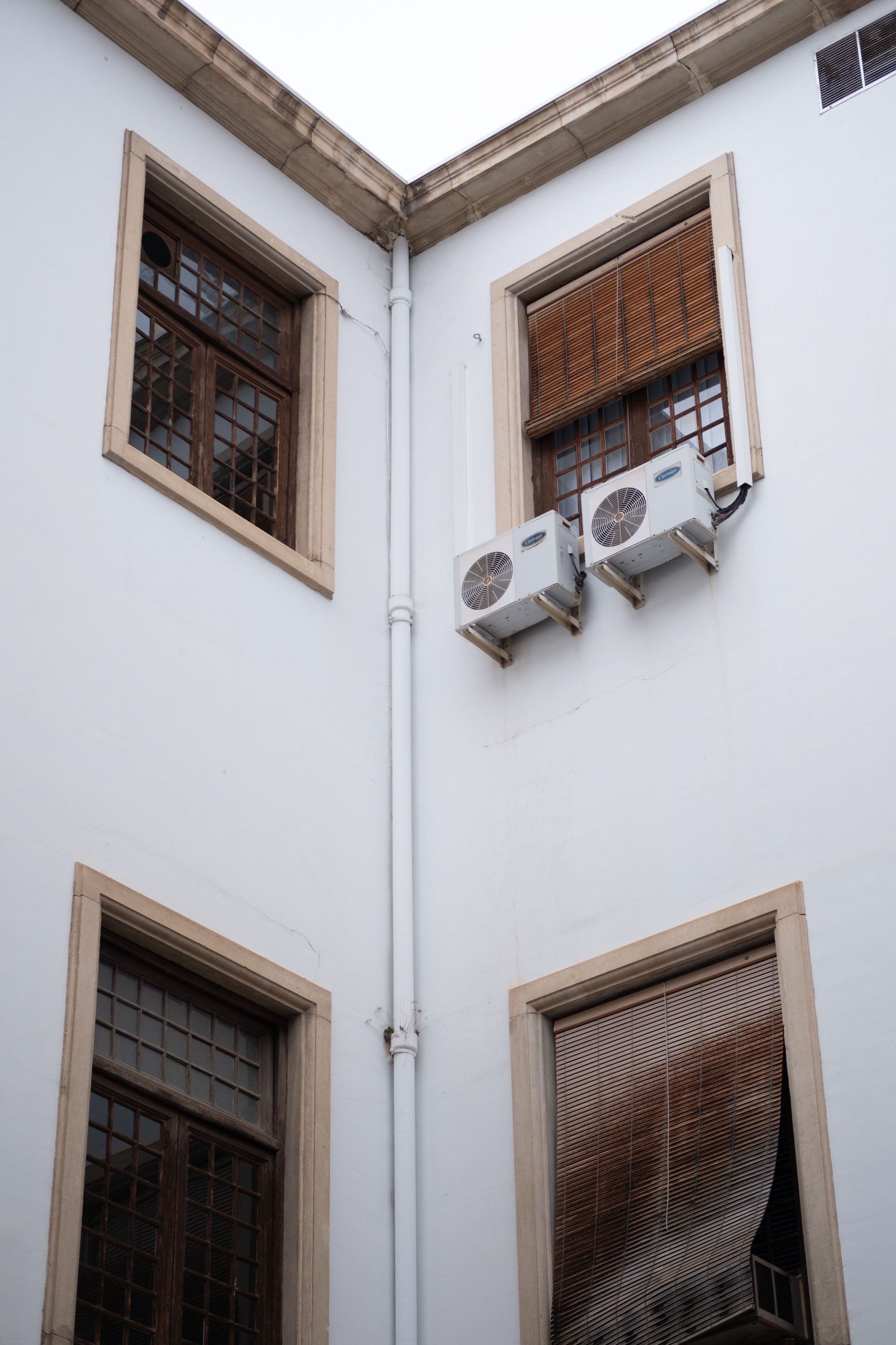 Corner of a white building with barred windows and two air conditioning units.