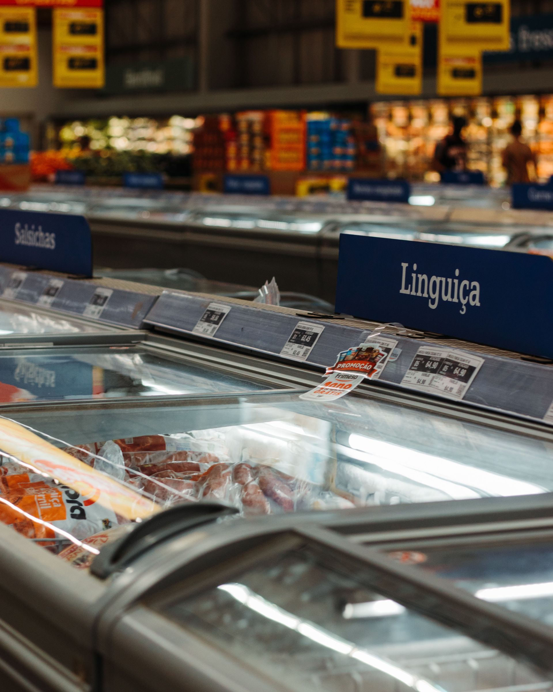 Supermarket freezer aisle with packaged meats and a “Linguiça” sign