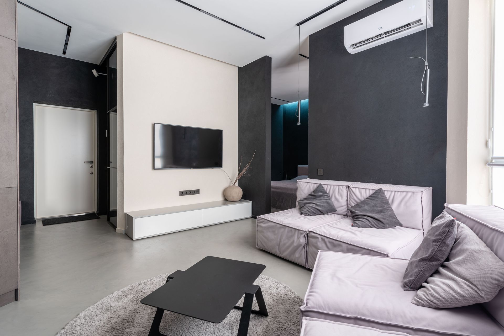 Modern living room with gray sofa, black coffee table, wall-mounted TV, and air conditioner