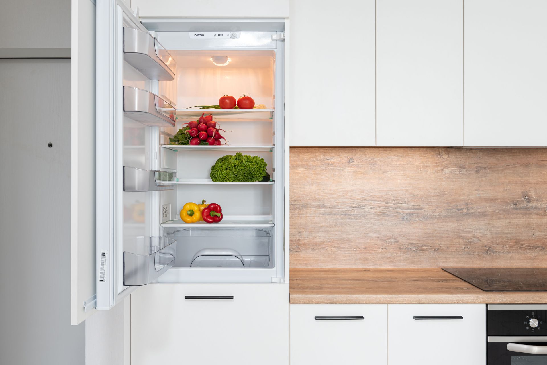 Open refrigerator in modern kitchen with shelves of fresh fruits and vegetables