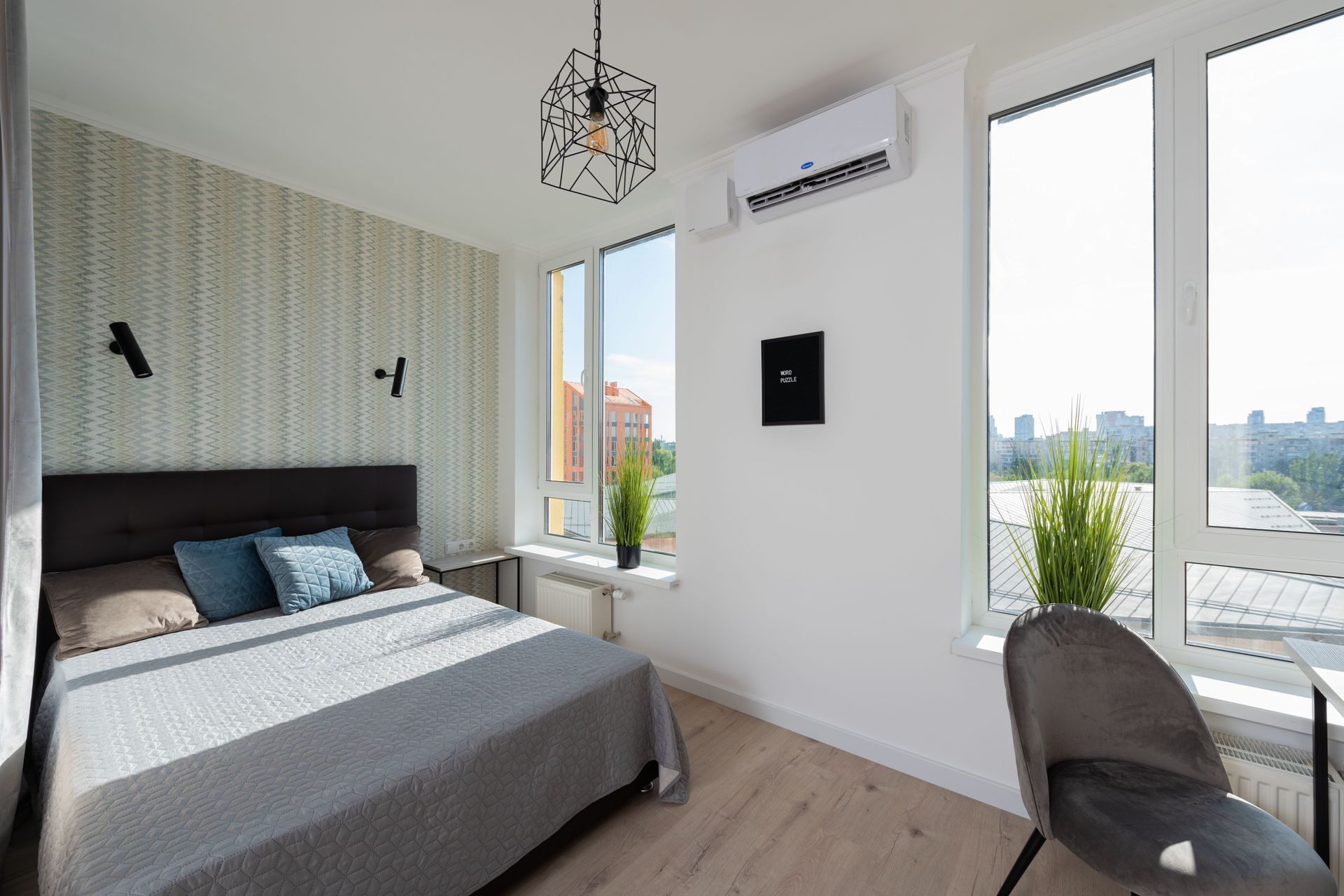 Bright modern bedroom with a bed, desk chair, large windows, and city view