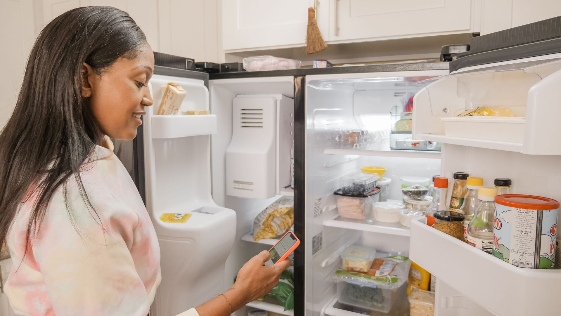 Woman opens a refrigerator and looks at food containers and jars inside.