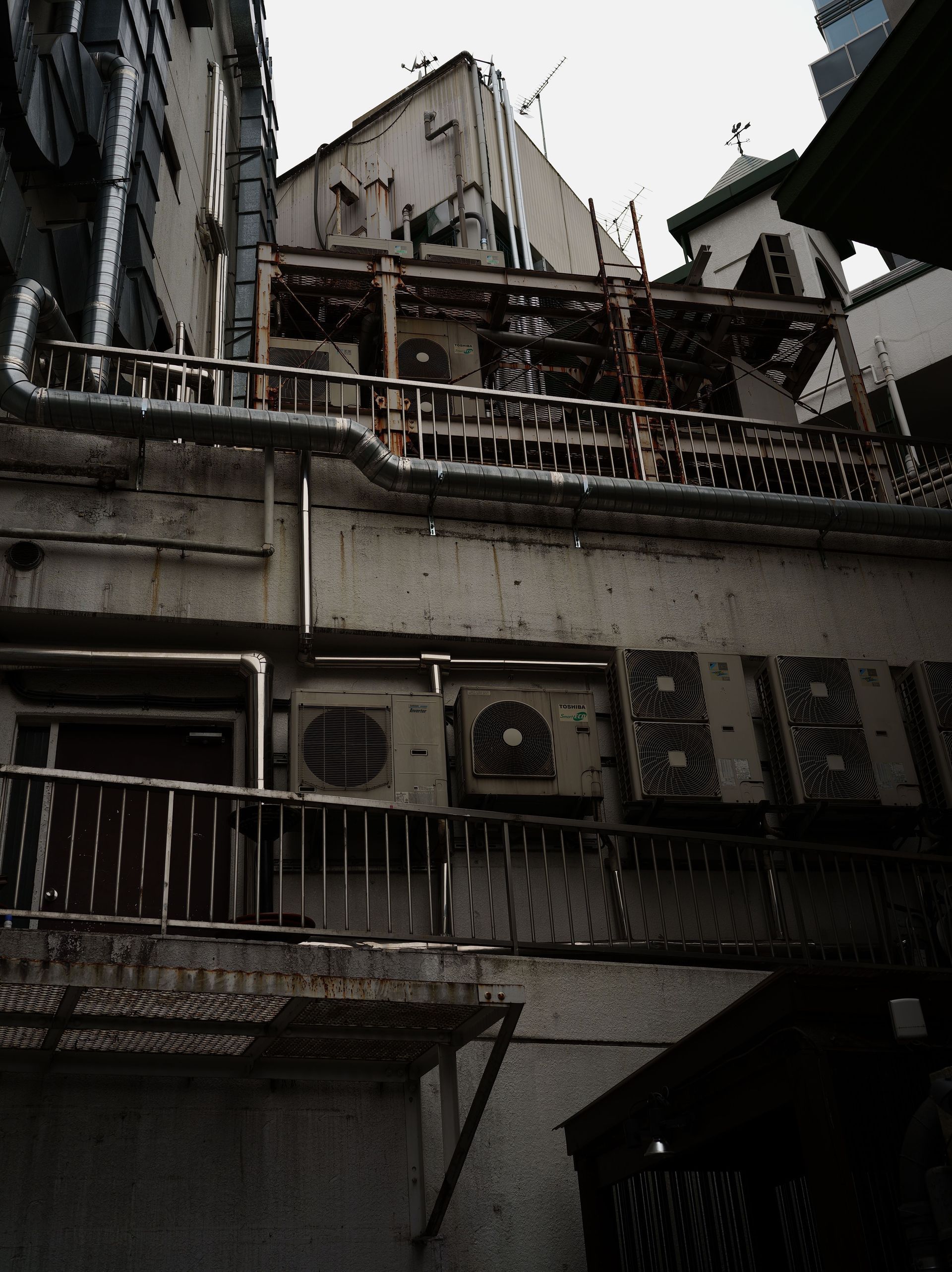 Narrow urban alley with weathered apartment buildings, balconies, railings, and air-conditioning units.