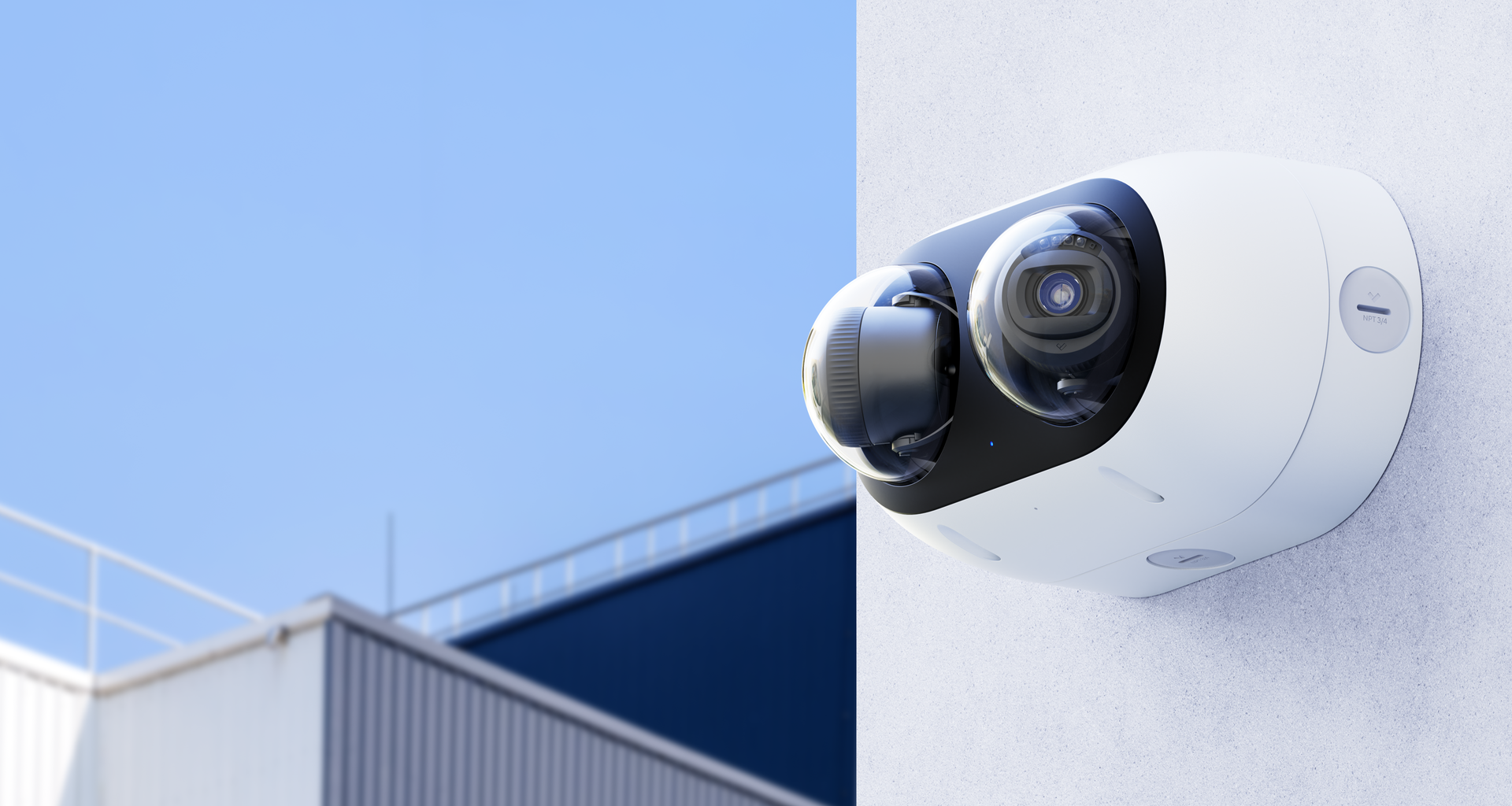 White security camera mounted on a wall; building and blue sky in background.