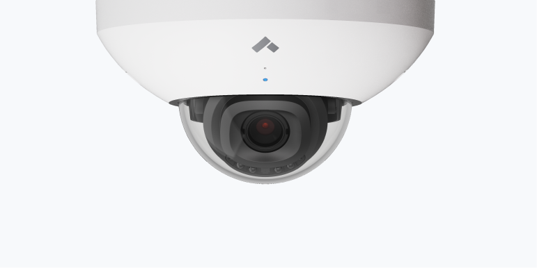 White security camera mounted on a wall bracket with a protective hood.