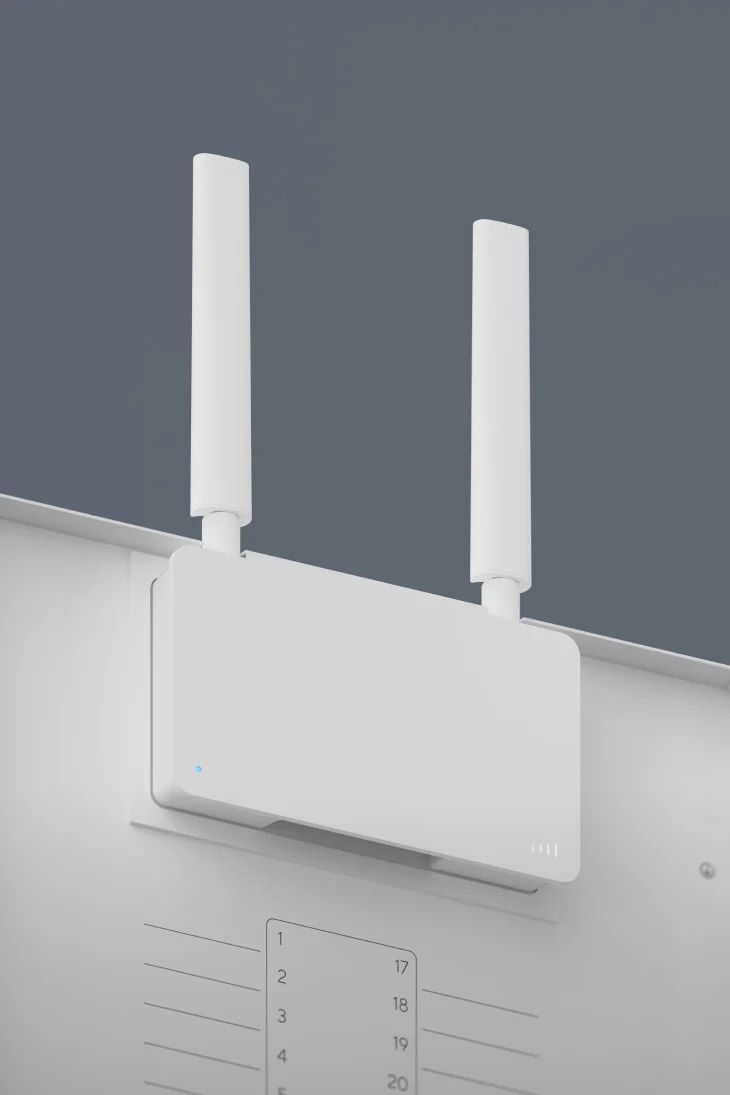 White Wi-Fi router with two vertical antennas mounted on a white surface against a blue-gray wall.