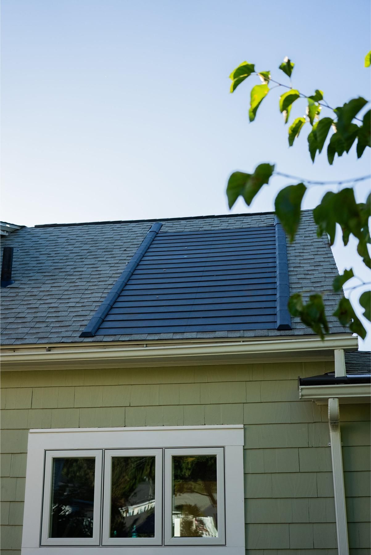 Green house with window and dark solar panels on the roof. Sunny day.