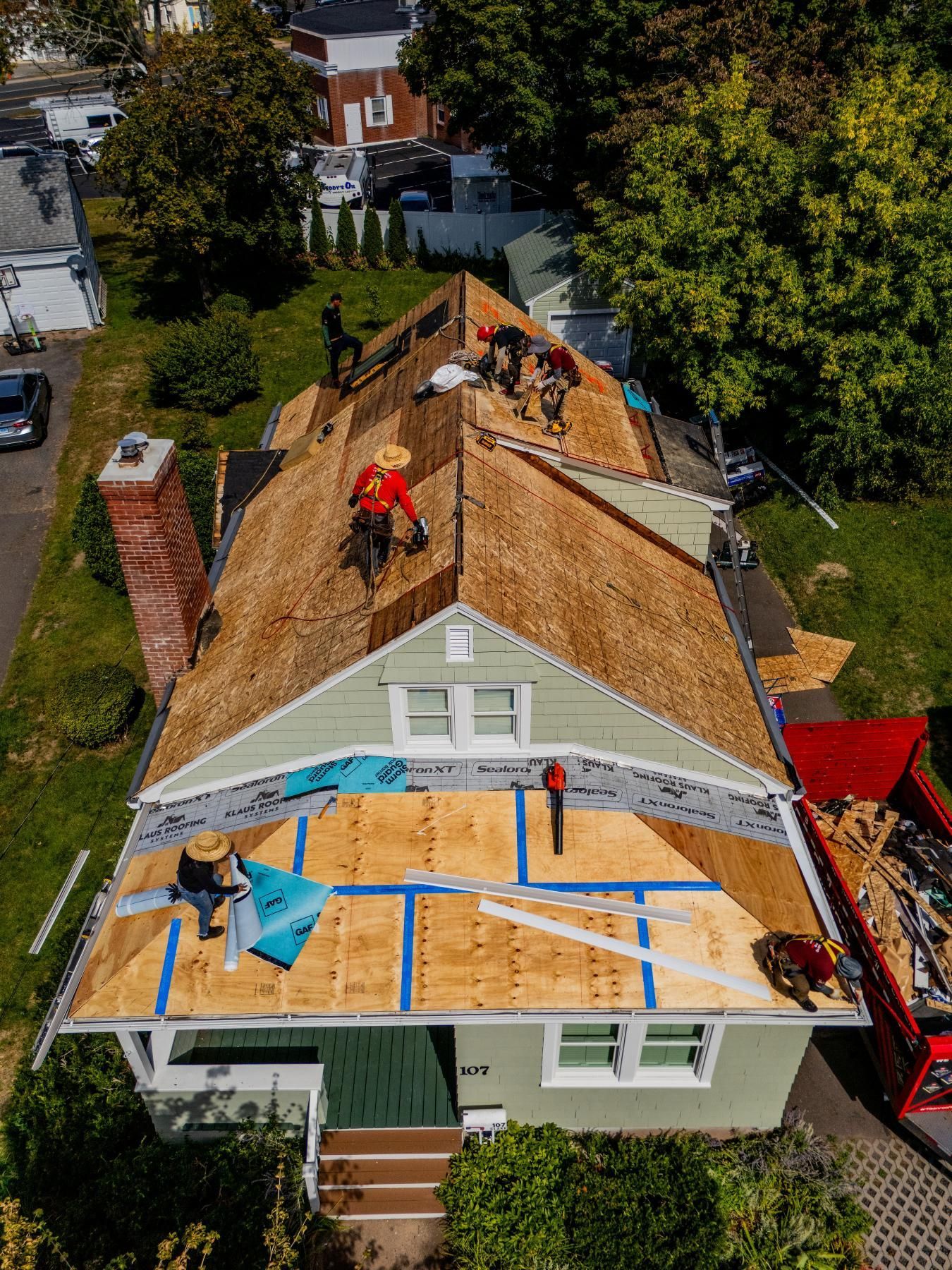 Roofers working on a house roof. Workers install shingles and underlayment on an old home with a brick chimney.