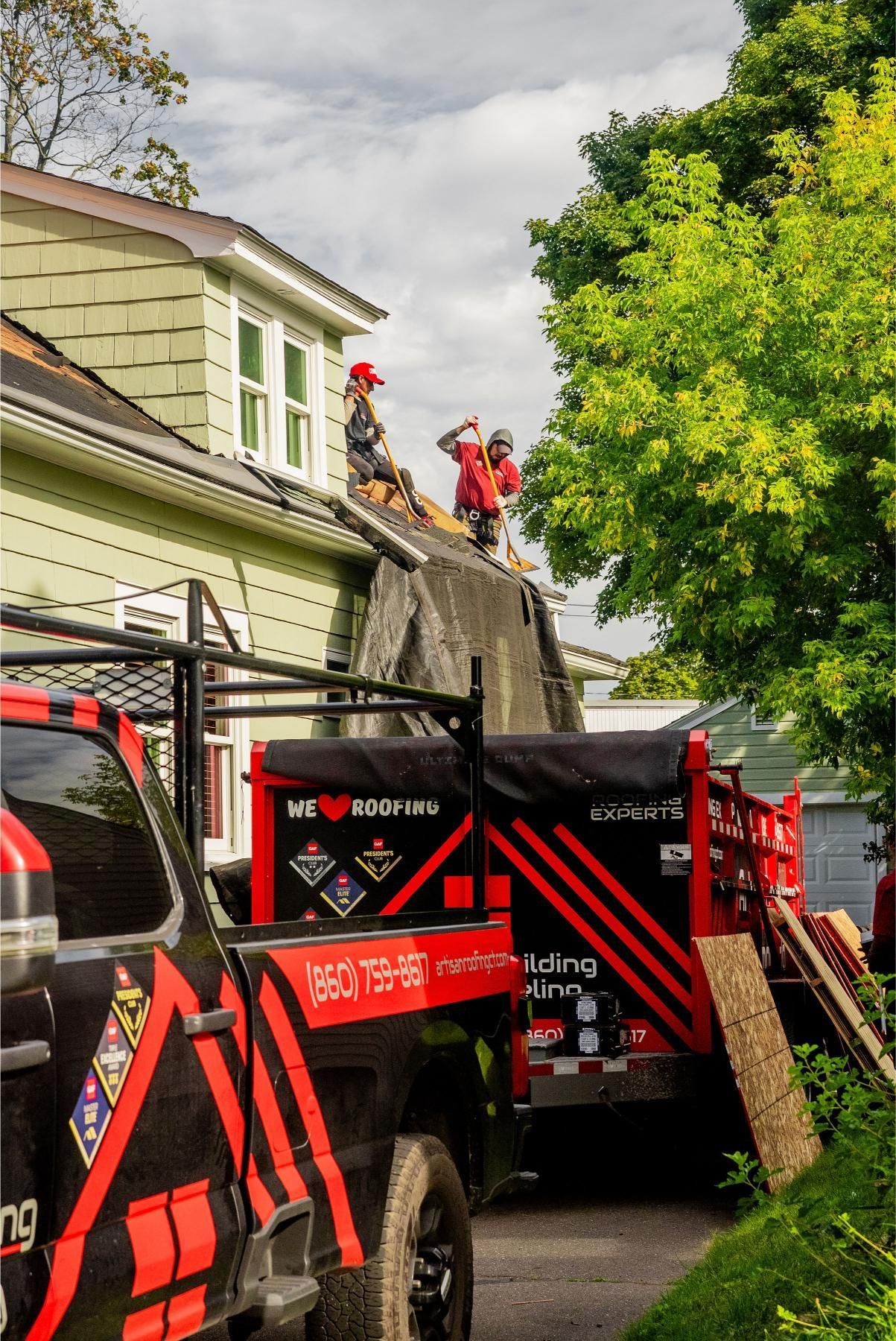 Roofers on a house roof. Red and black truck parked below.