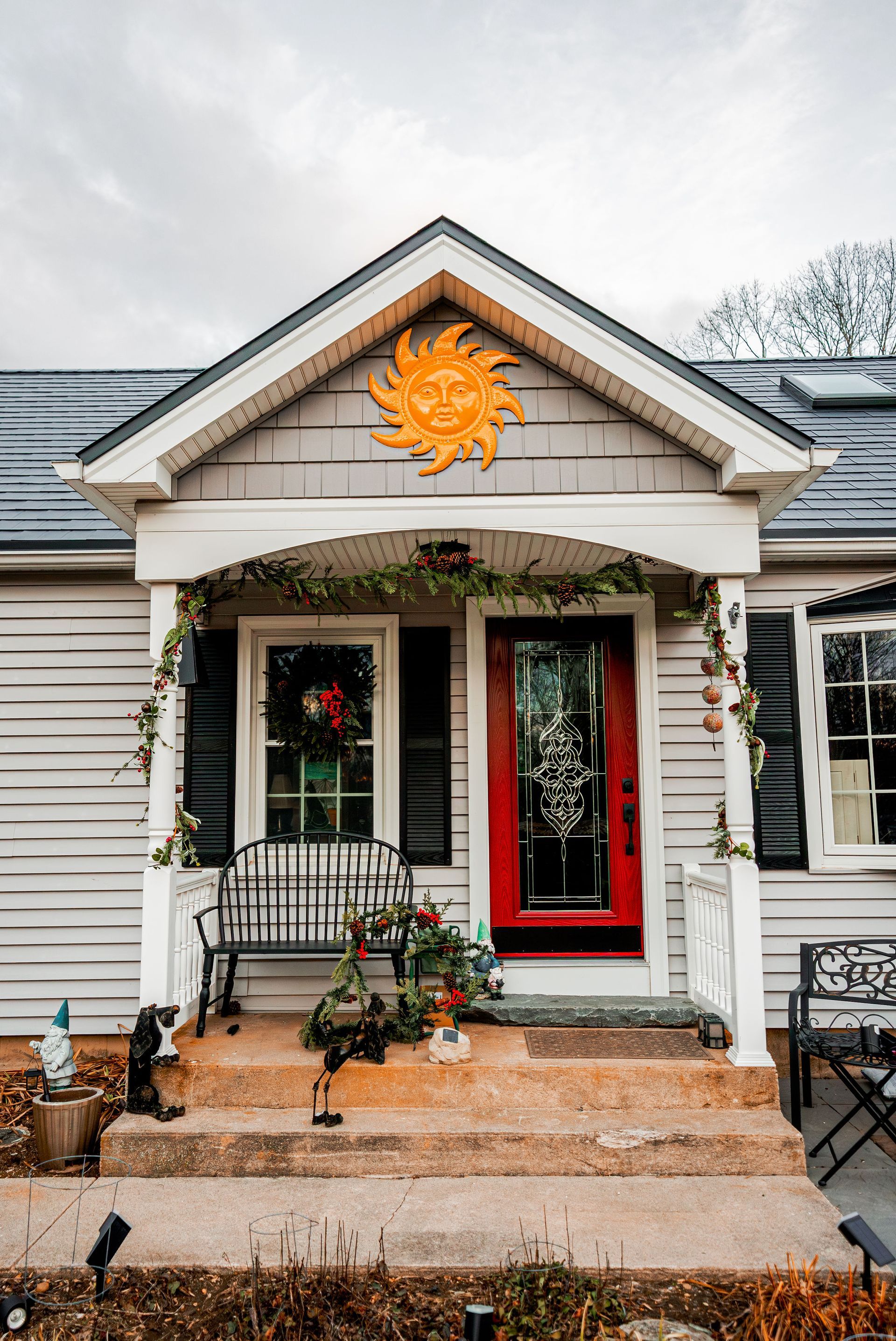 Small house with red door and porch decorated with greenery. A sun decoration is above the door.