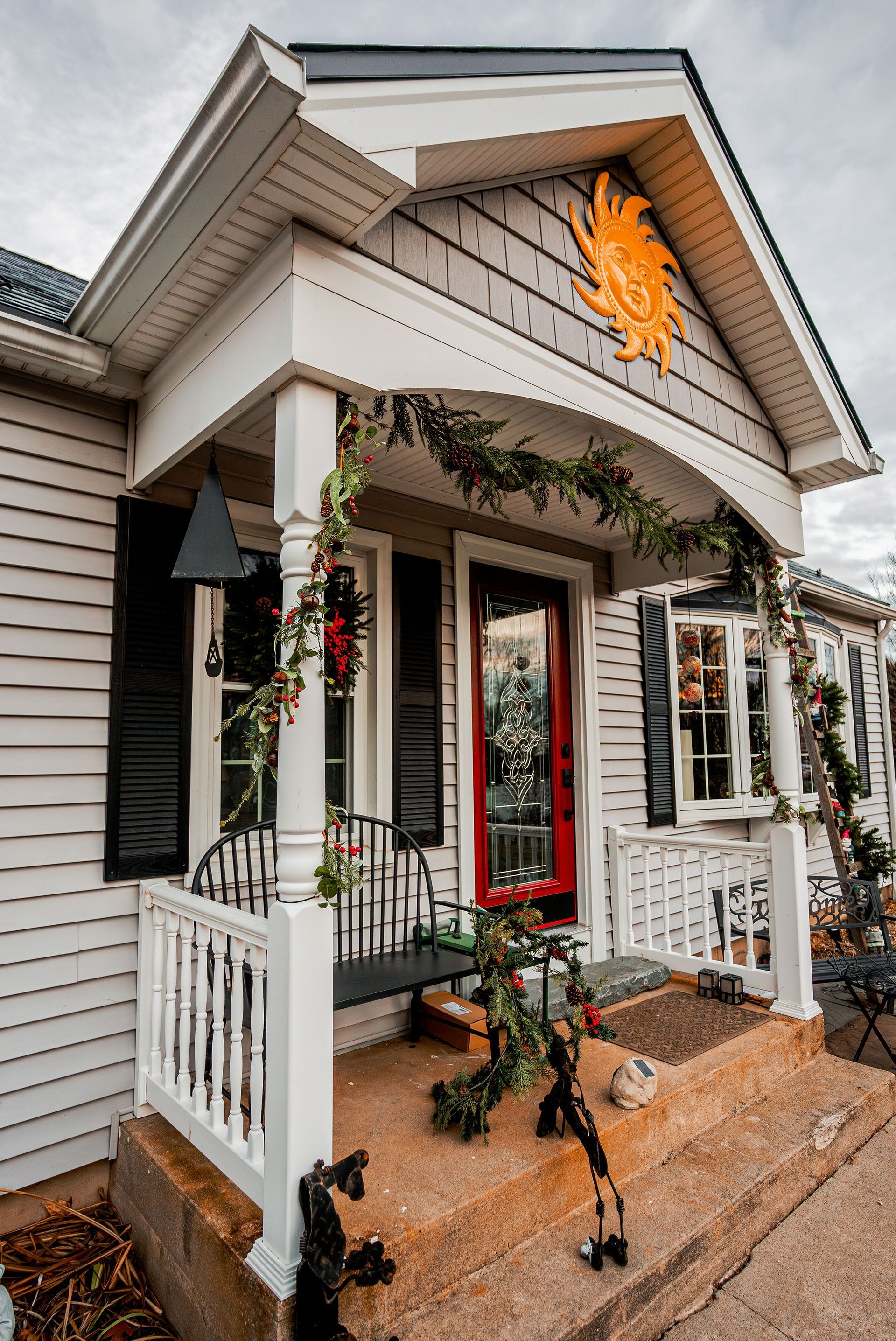 White house with red door, decorated with garland. Black shutters, porch with bench.