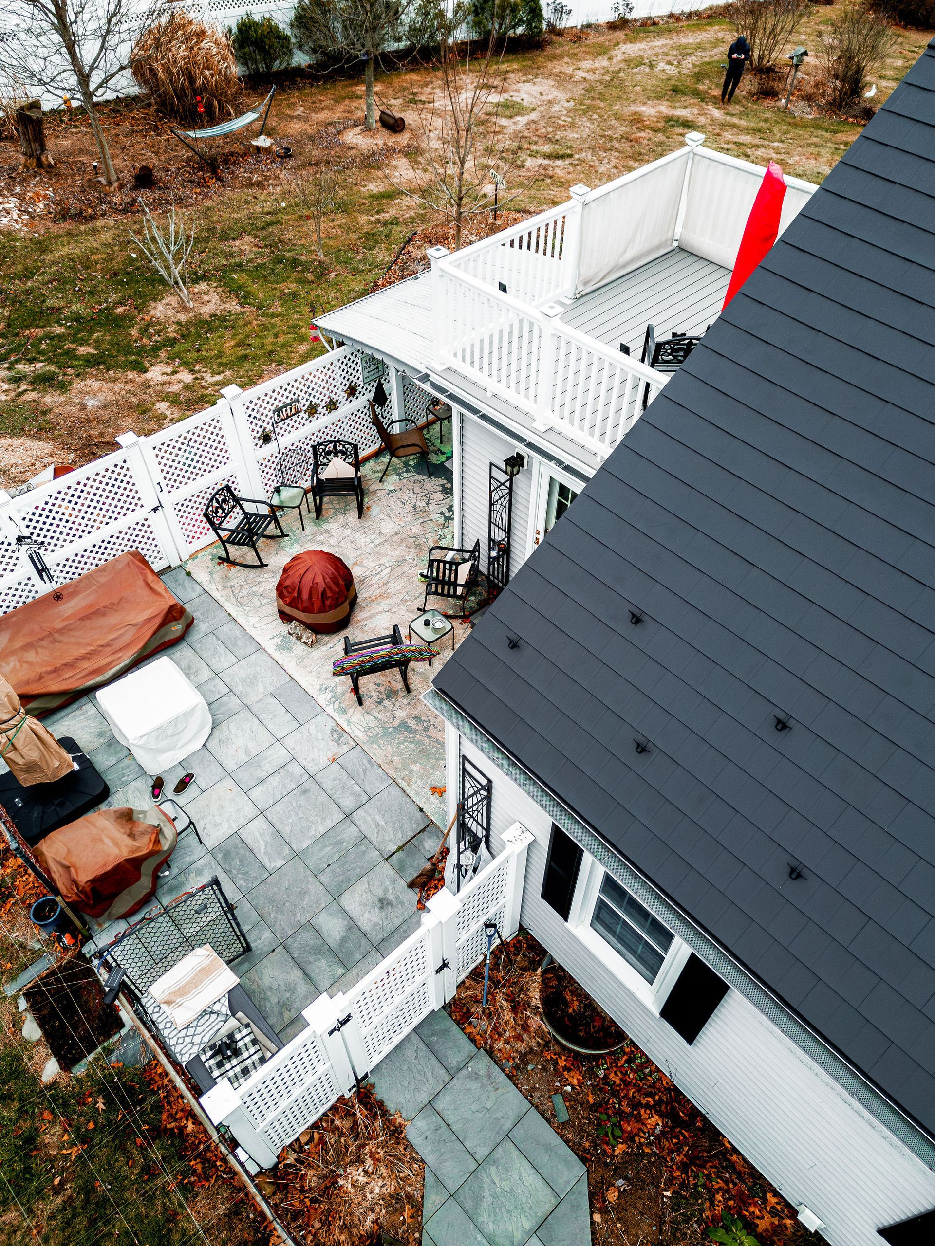 Overhead view of a white home with a gray roof and patio. Patio has seating and a fire pit.