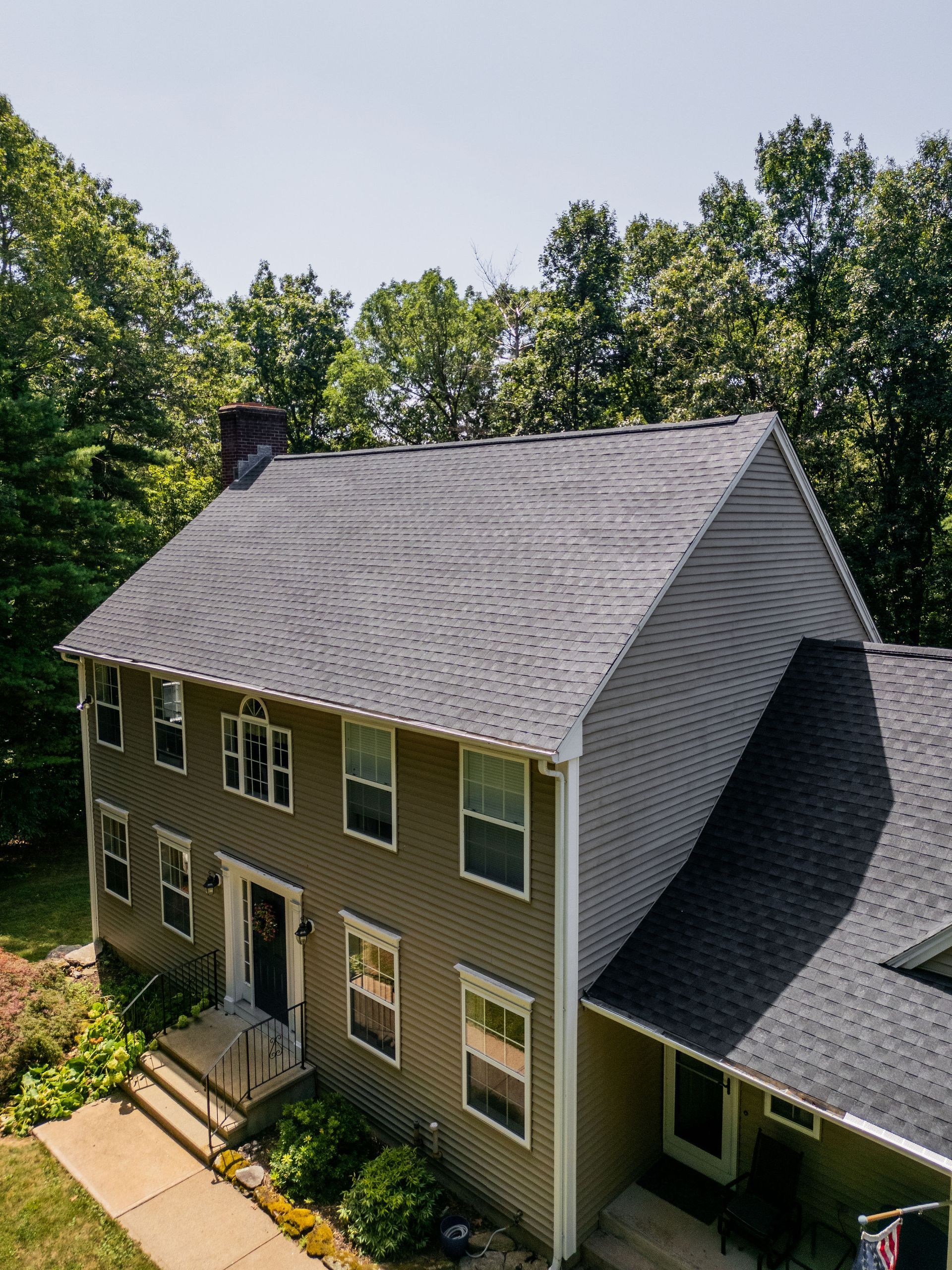 Two-story house with gray roof and siding, surrounded by trees on a sunny day.