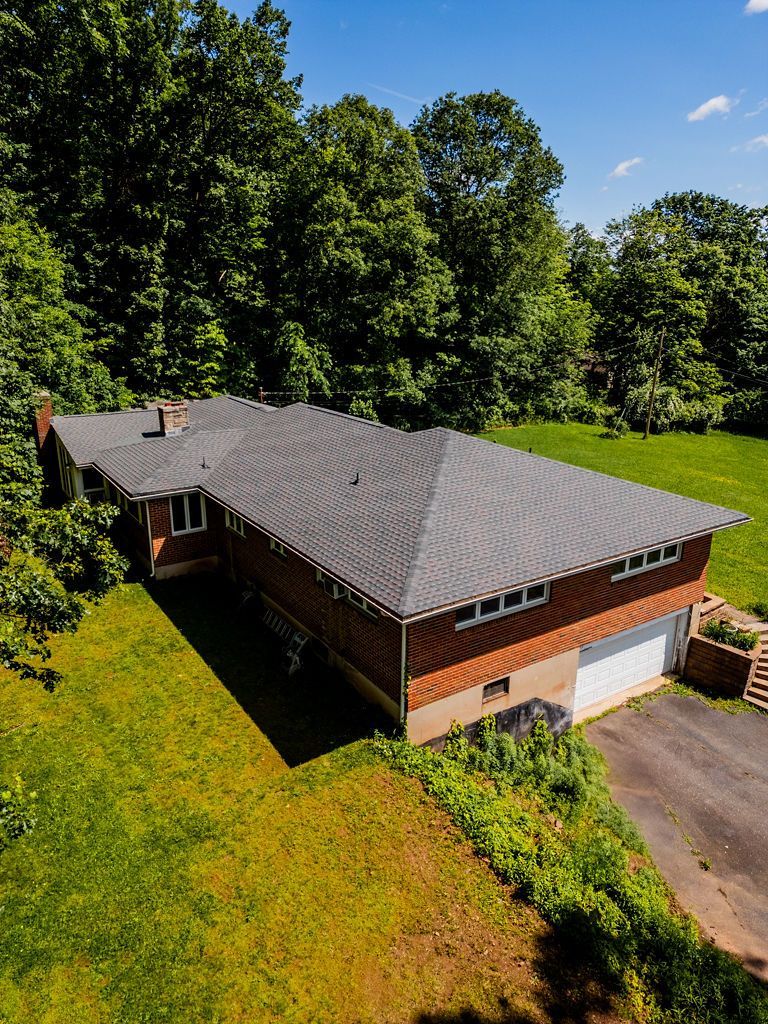 Brick house with dark roof and attached garage, surrounded by green lawn and trees under a blue sky.