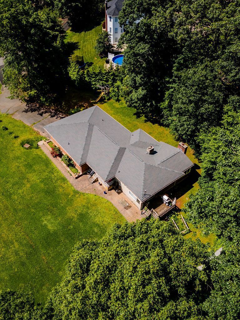 Overhead view of a house with a gray roof, surrounded by green trees and grass, on a sunny day.