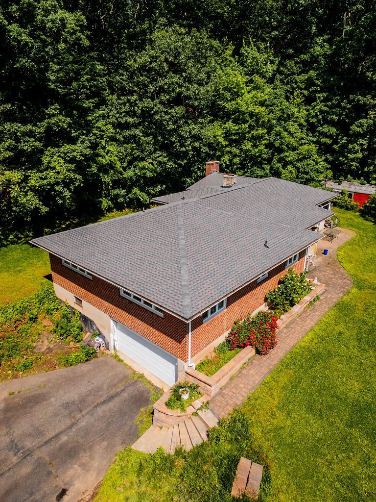 Aerial view of a one-story brick house with a dark gray roof surrounded by green trees and grass.