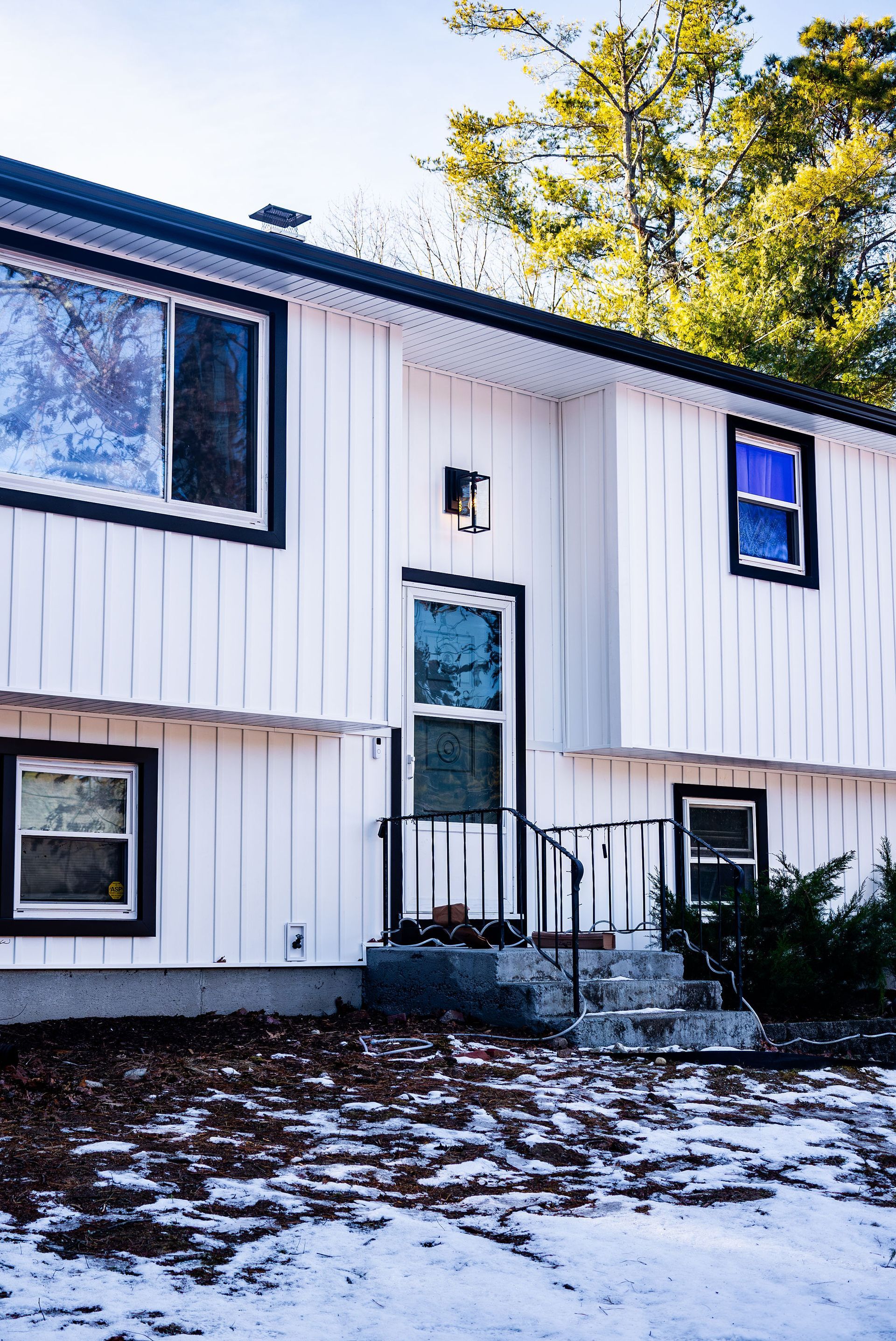 White two-story house with black trim, entry door, windows, and small porch. Snow covers the ground.