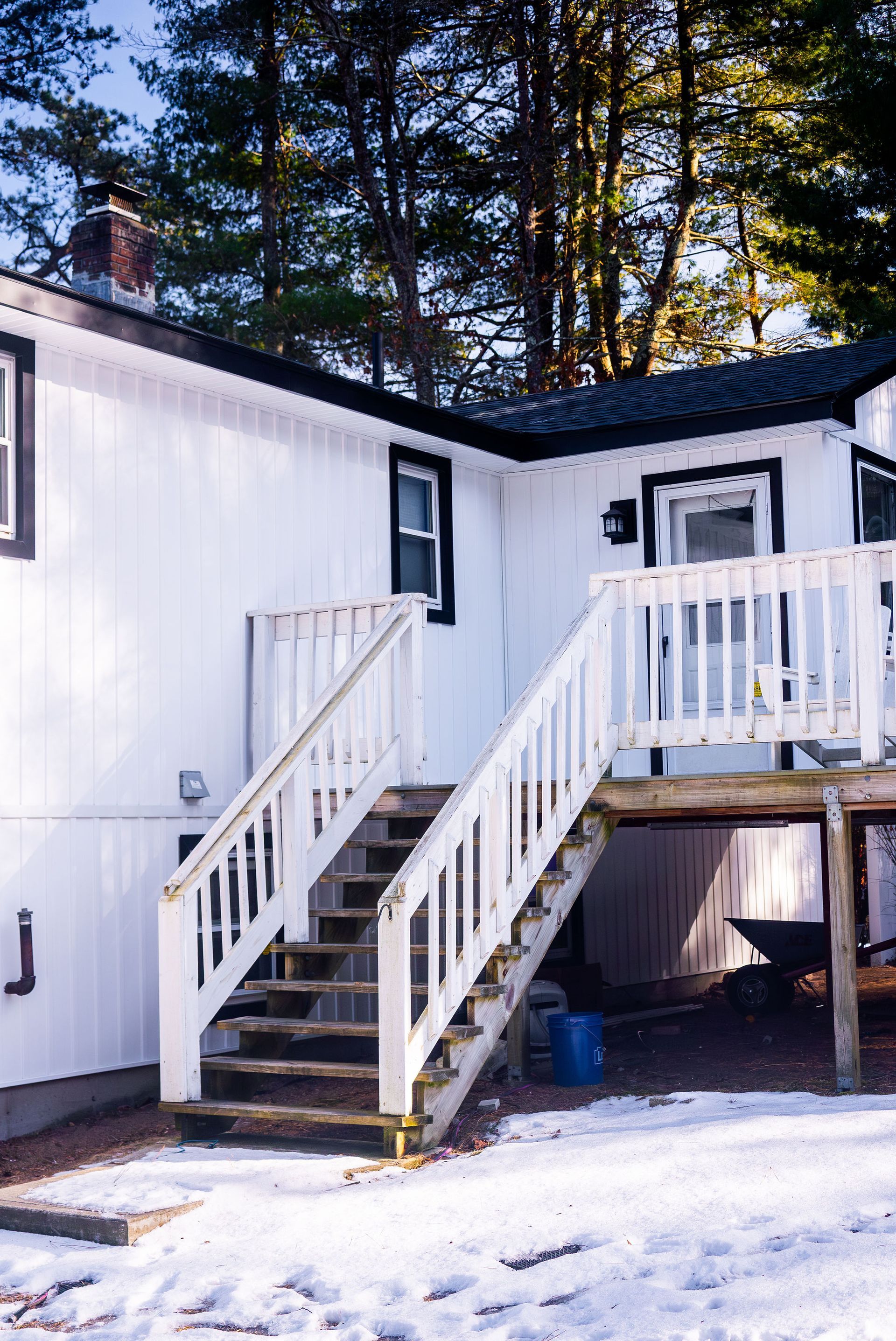 White house with wooden stairs and deck; snow on ground.