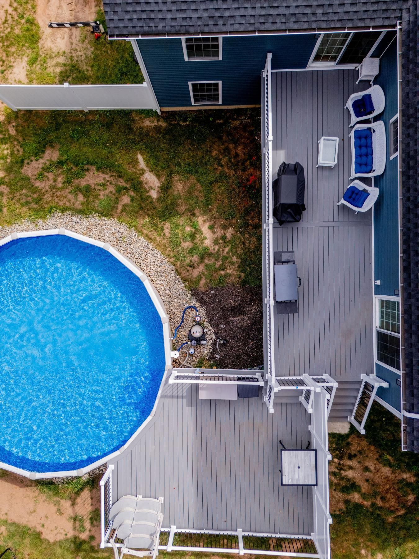 Aerial view of a backyard with a pool, deck, and house. Blue pool, gray deck, white furniture.